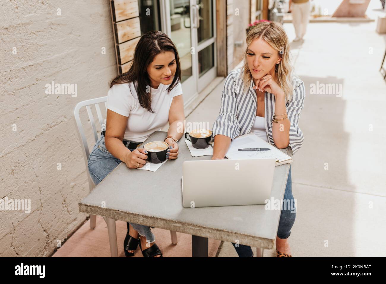 Zwei junge weibliche Berufstätige arbeiten gemeinsam draußen auf einem Laptop Stockfoto