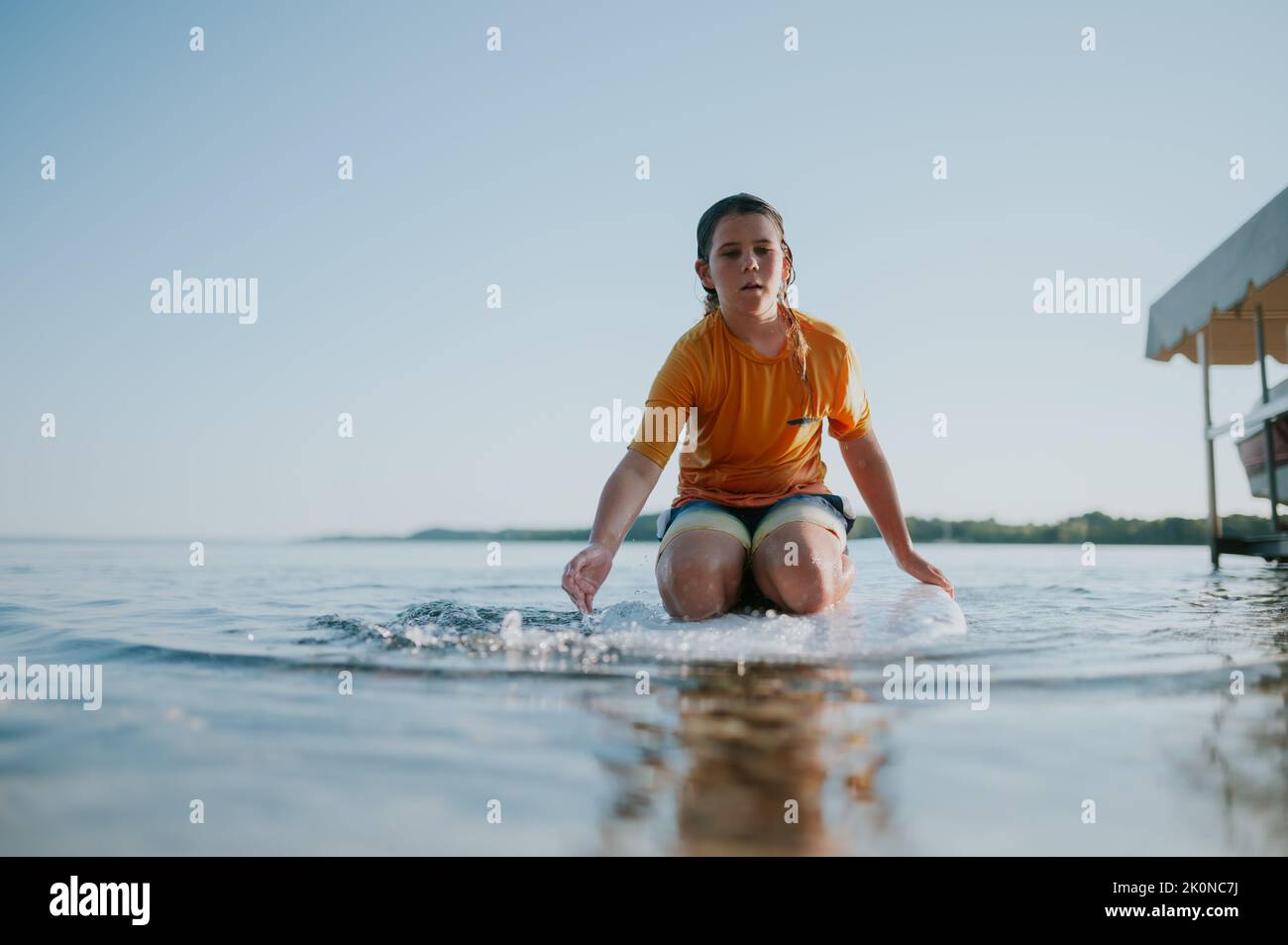 Blick aus der unteren Perspektive auf einen Jungen, der auf dem Paddelbrett sitzt und in Richtung des Betrachters paddelt Stockfoto