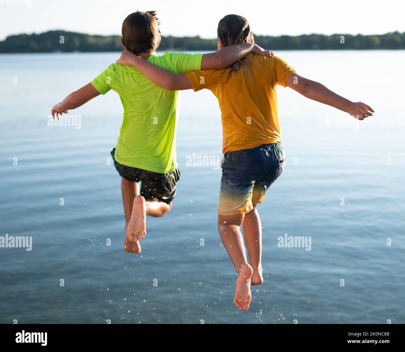 Die Jungen springen Arm in Arm von einem Dock ins ruhige Wasser bei Sonnenuntergang Stockfoto