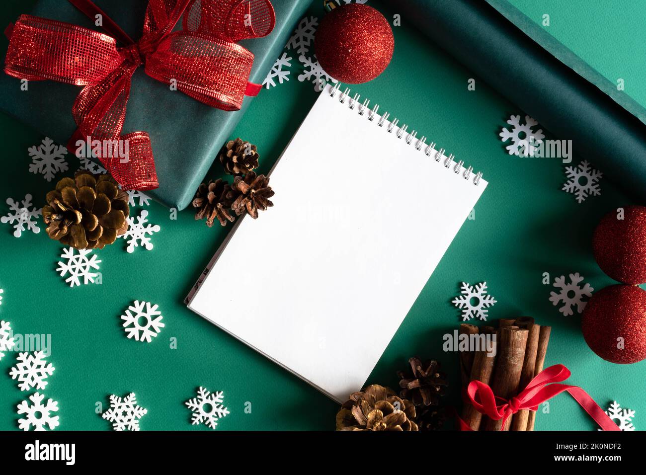 Weihnachtliche Naturdekorationen aus Holz, rote Kugeln, Geschenkbox und Notizblock auf grünem Hintergrund. Weihnachtsgruß-Design. Flach liegend, Draufsicht, Kopierbereich. Das Konzept von Urlaub und Neujahr. Stockfoto