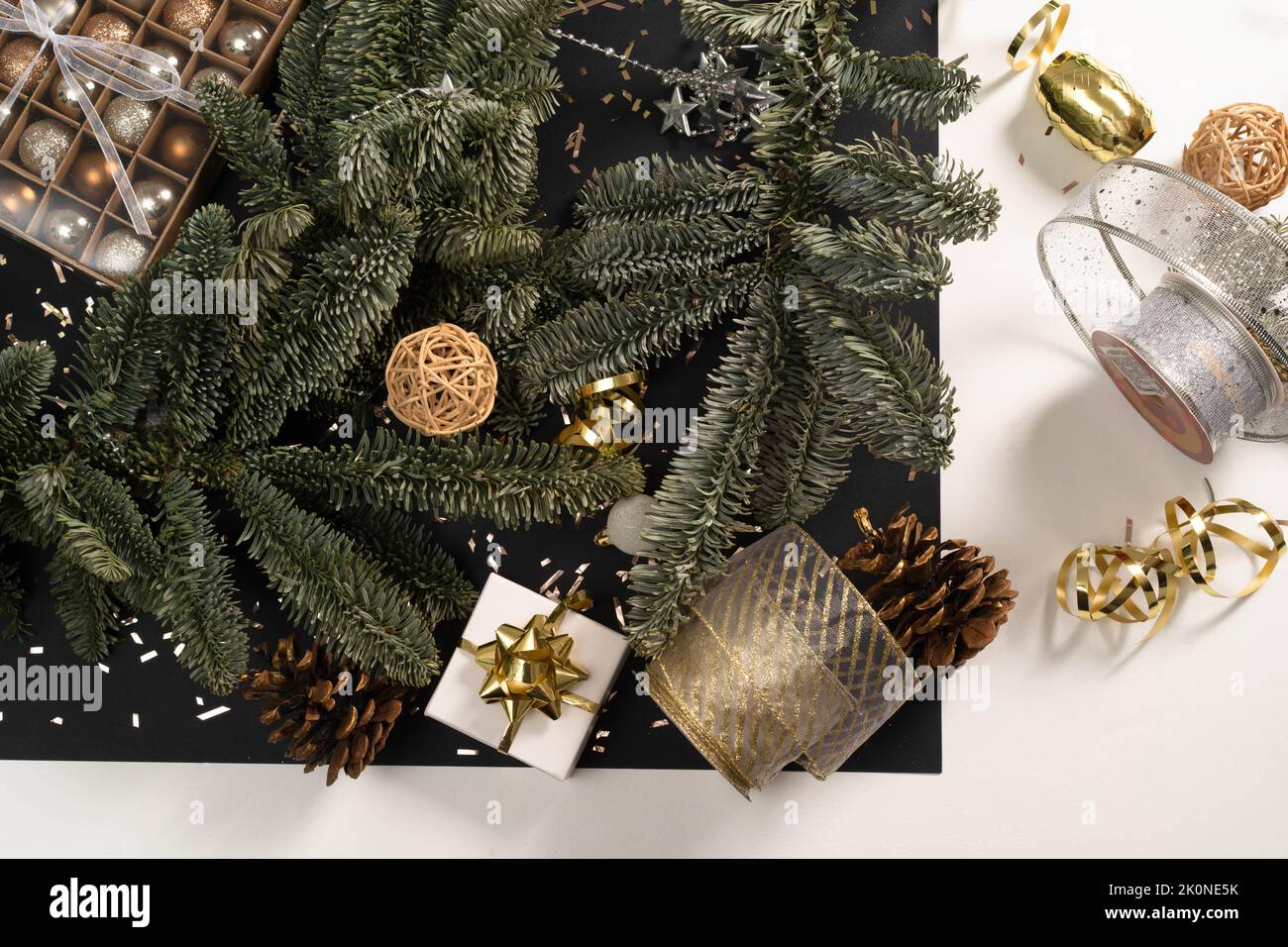 Tannenkranz und Weihnachtsdekor auf schwarz-weißem Hintergrund. Vorbereitungen für Weihnachten, Postkarte, Weihnachtskugeln, Geschenkboxen, Bänder. Flaches Lay, eleganter Stil, Urlaub. Stockfoto