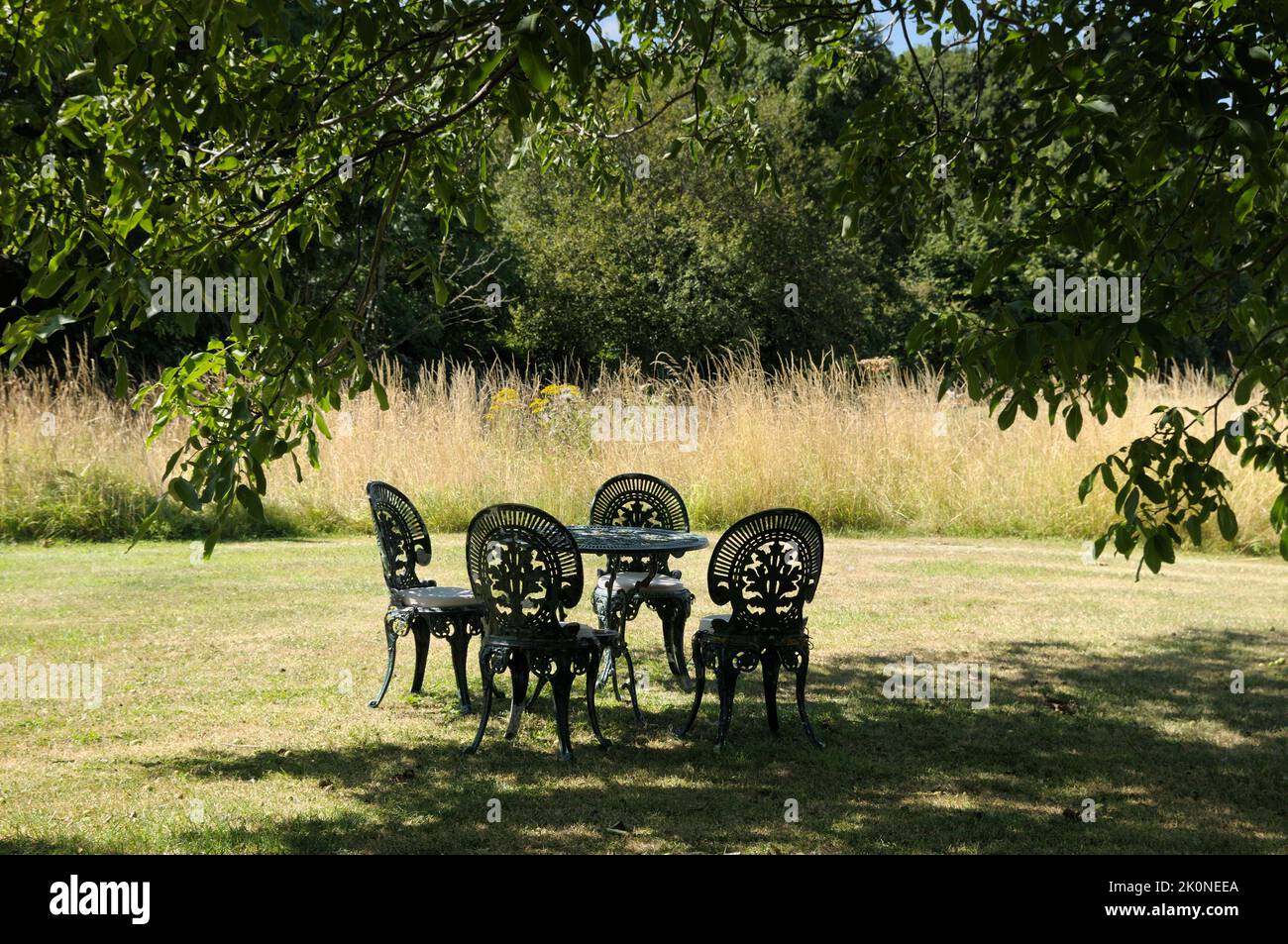 Ein Satz von grün verzierten Metalltischen und Stühlen auf einem Rasen unter dem Schatten eines Baumes in einem ländlichen Garten im Sommer. England, Großbritannien Stockfoto