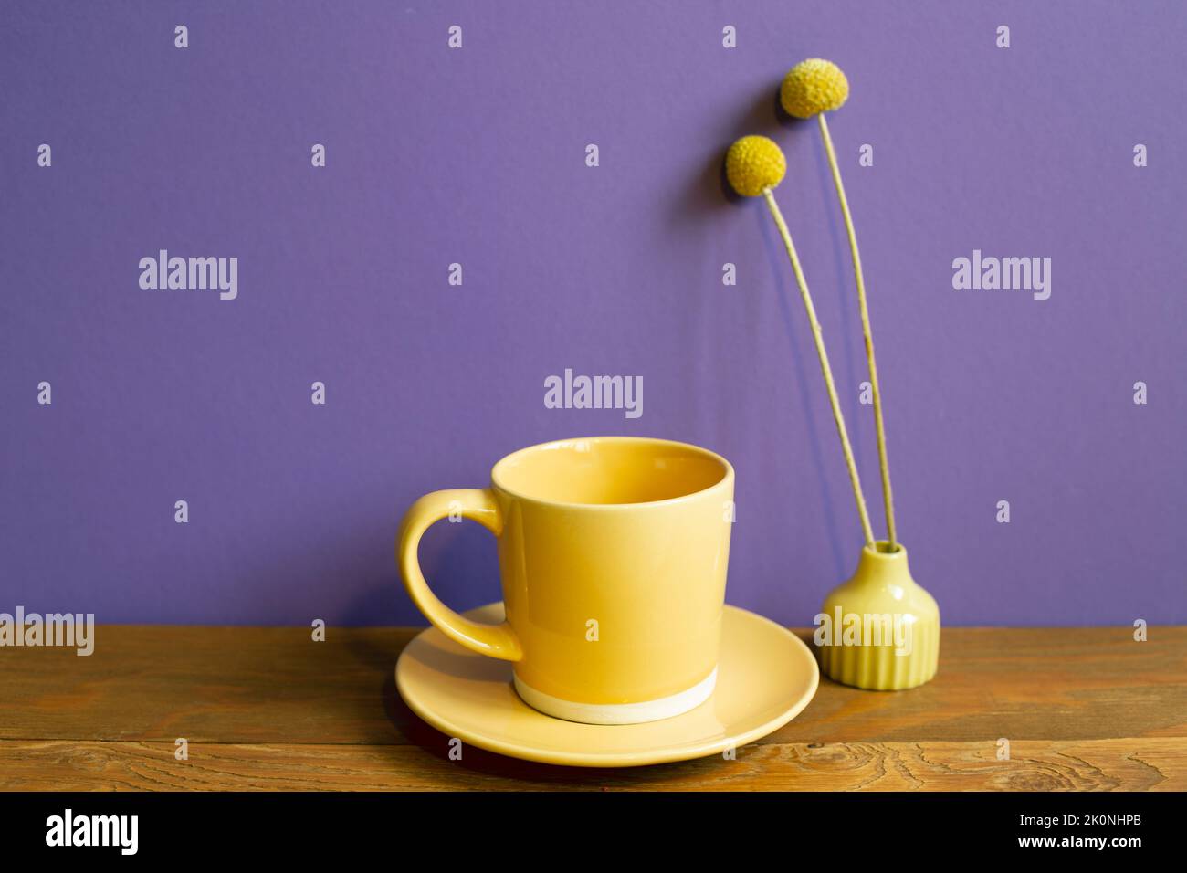 Gelbe Kaffeetasse und trockene Blume auf Holztisch. Lila Wandhintergrund. Retro-Stil Stockfoto