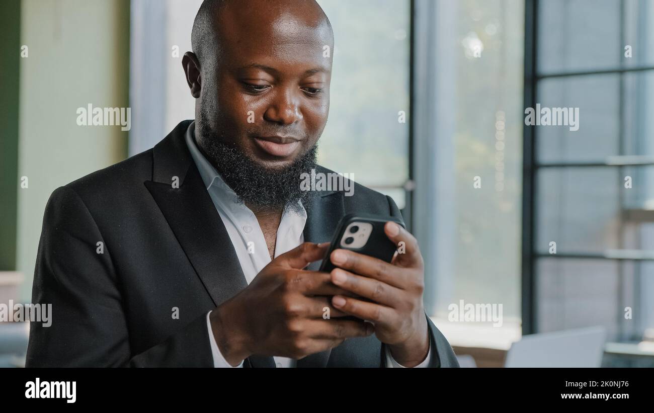 afroamerikanischer Erwachsener Geschäftsmann bärtiger männlicher Angestellter chattet in Zelle App halten Mobiltelefon hochladen Geschäftsinformationen scrollen Internetseiten machen Stockfoto