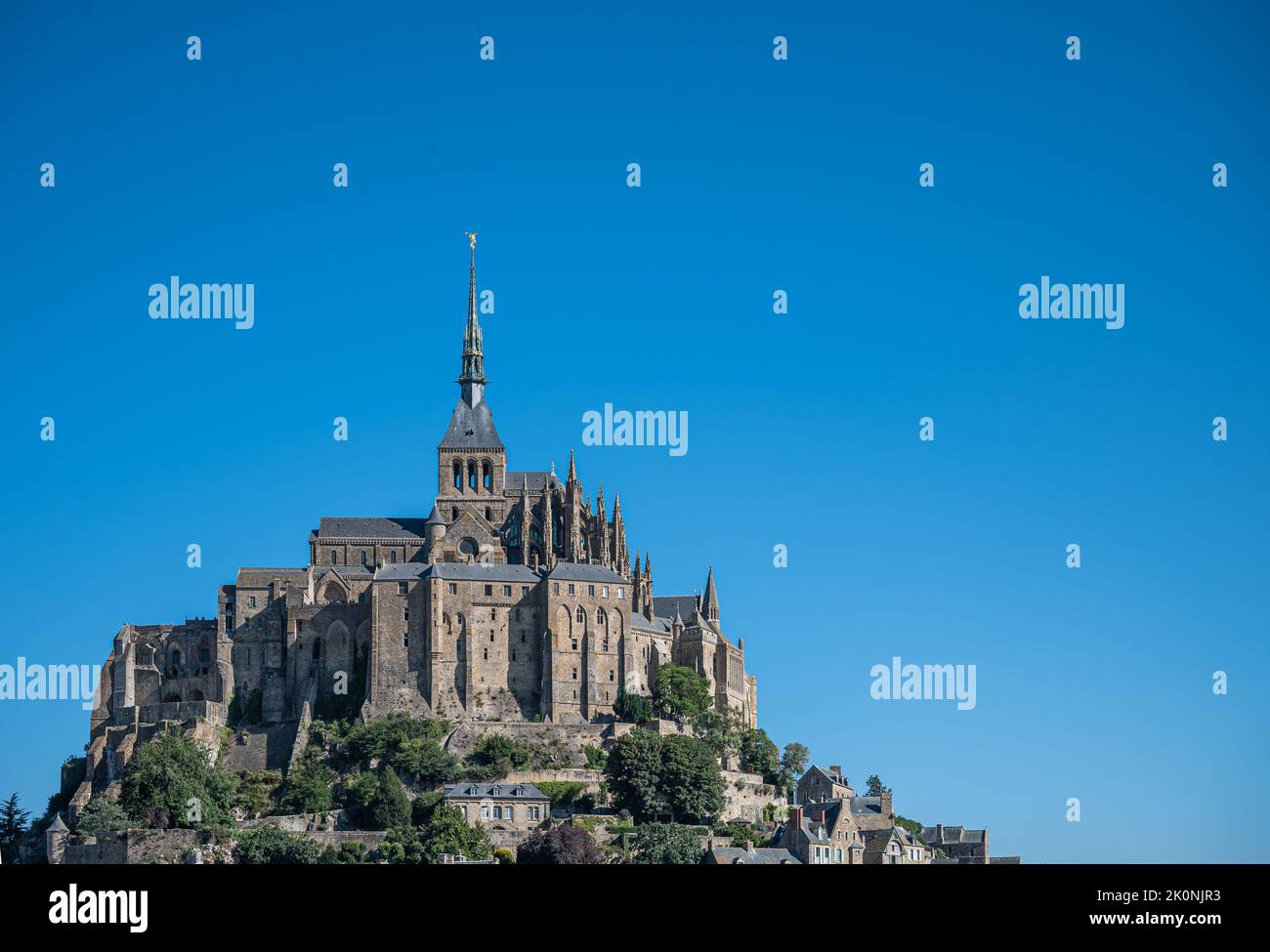 Mont St. Michel, Normandie, Frankreich - 8. Juli 2022: Historischer Abteiteil aus braunem Stein mit Kirche auf Felsen gegen blauen Himmel. Etwas grünes Laub auf f Stockfoto