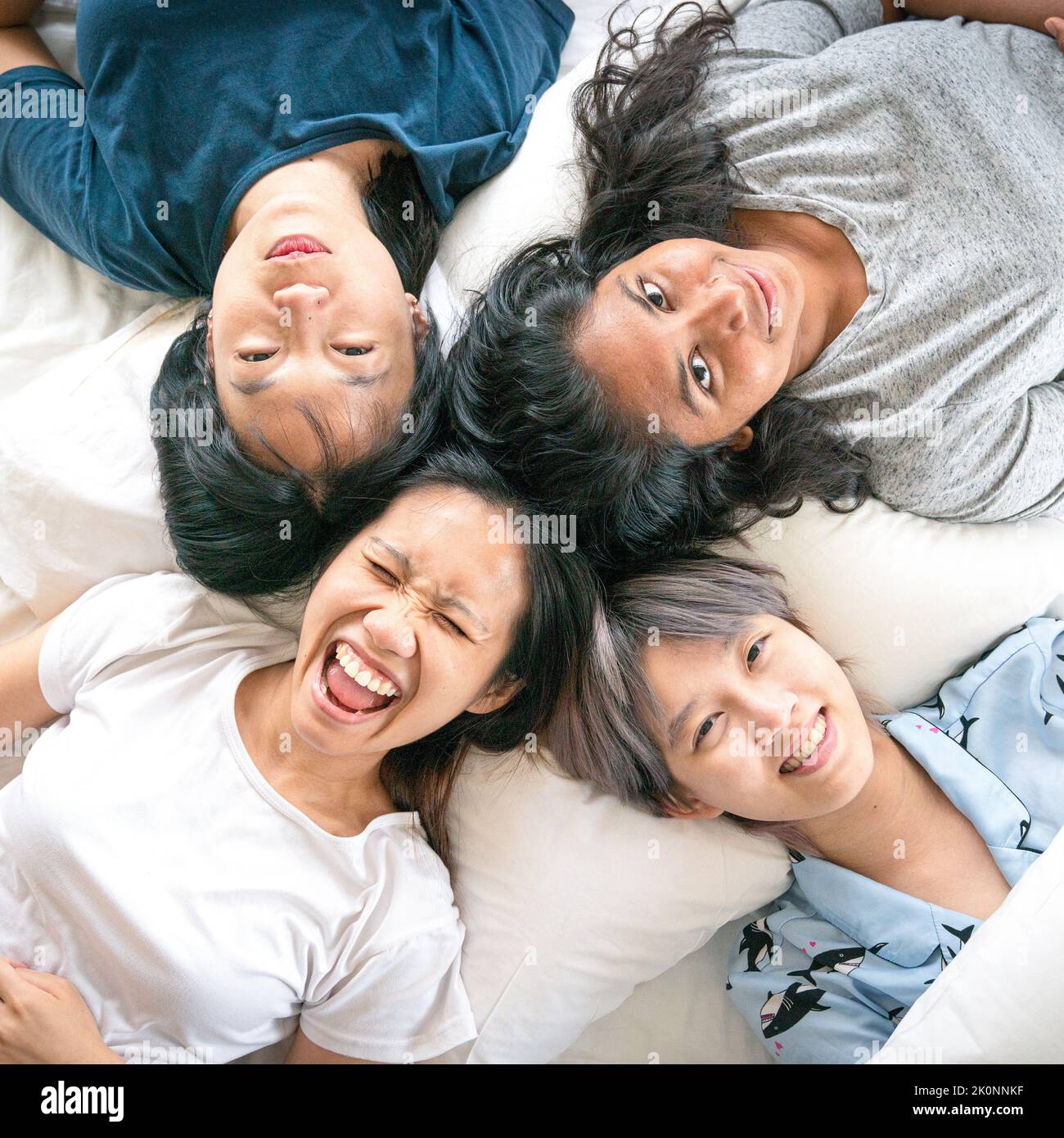 Glückliche, multiethnische junge Frauen liegen im Bett, lächeln und lachen. Draufsicht. Stockfoto
