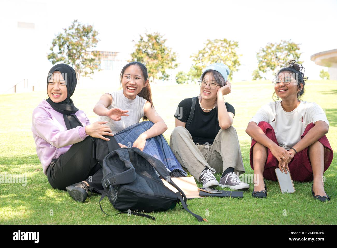 Eine Gruppe von vier jungen asiatischen Frauen, die auf grünem Rasen sitzen und miteinander reden und lachen. Studenten mit Treffen und gelegentliche Diskussion im Freien CO Stockfoto