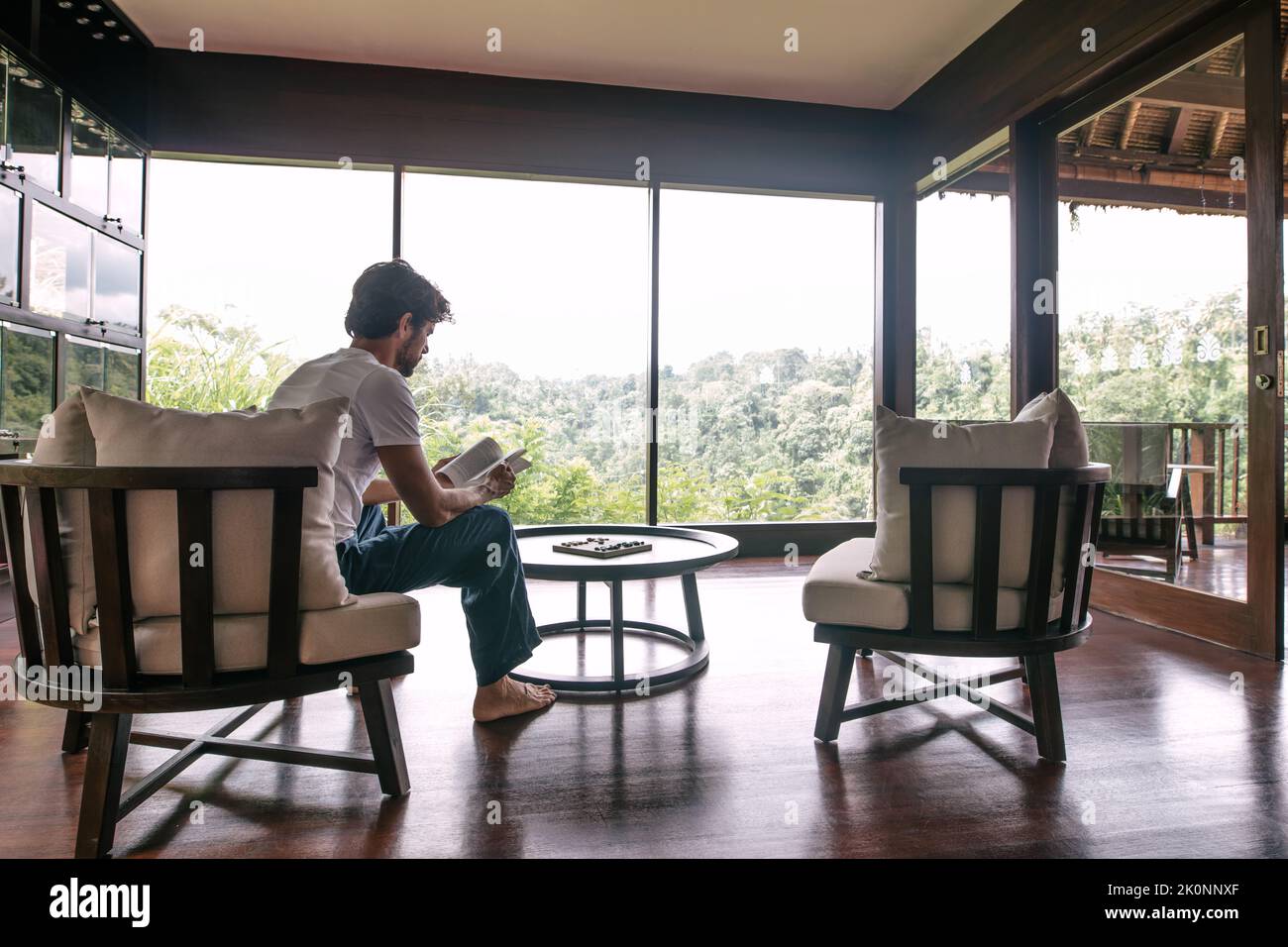 Innenaufnahme eines jungen Mannes, der in einem Hotelzimmer sitzt und ein Buch liest. Stockfoto