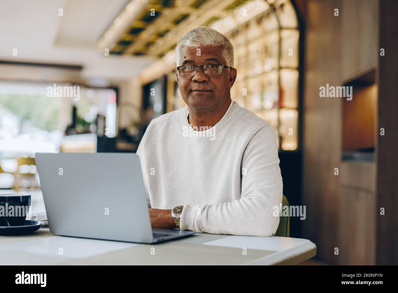 Leitender Geschäftsmann, der in einem modernen Café auf die Kamera schaut. Ein reifer Geschäftsmann, der einen Laptop verwendet, während er aus der Ferne arbeitet. Stockfoto