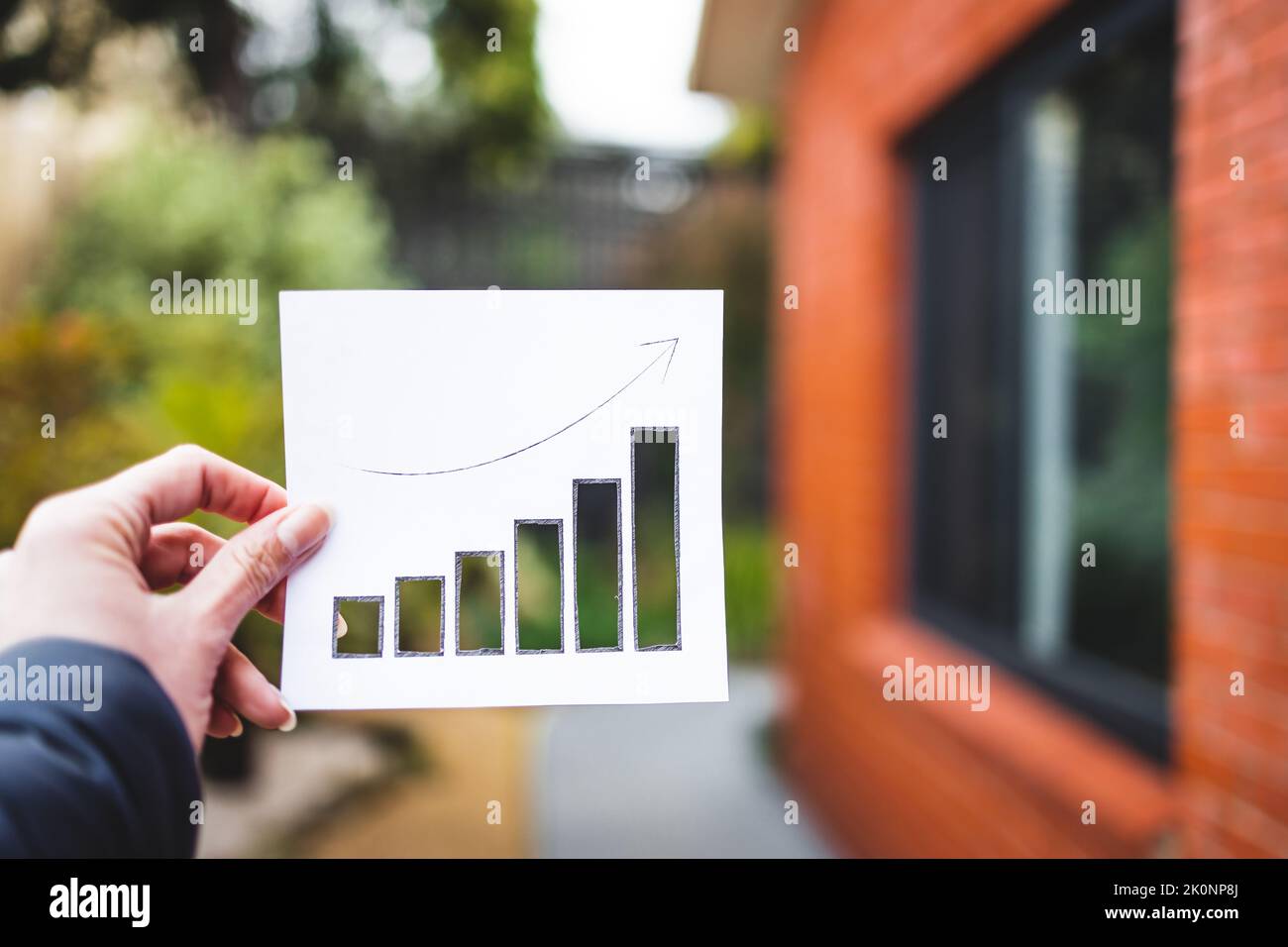 Immobilienwert und Rendite auf Investitionen oder Mietpreis konzeptionelles Bild, Hand halten Immobilien-Grafik zeigt Statistiken nach oben mit Ausschnitten vor o Stockfoto