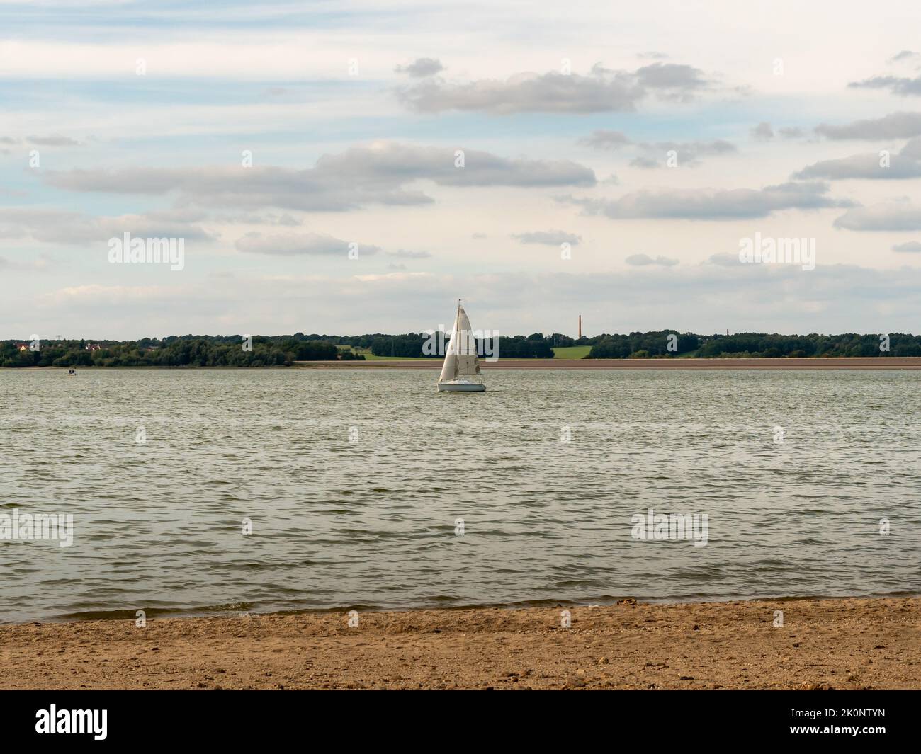 Segelboot auf einem See in Deutschland. Weißes Schiff mit großem Segel auf ruhigem Wasser. Transport auf dem Wasser. Naturlandschaft mit einem Boot in der Mitte. Stockfoto