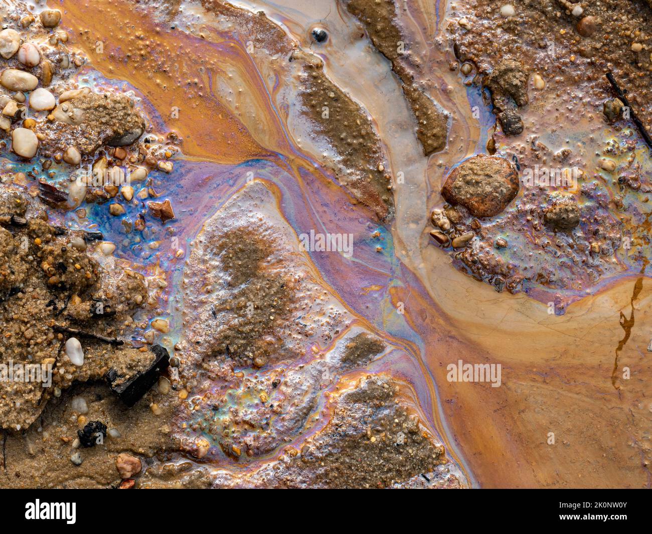 Verschmutzung durch Ölverschmutzungen im Wasser und auf dem Sand. Fossile Brennstoffe in der Umwelt. Spektrale Lichtfarben sind sichtbar. Die Natur ist kontaminiert. Stockfoto