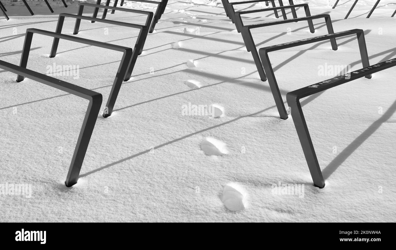 Fußspuren im Schnee folgen einem eingleisenden Pfad zwischen Geländern, Sonnenlicht hebt die Schatten der Geländer hervor, Geländer sind symmetrisch über die Fußspuren Stockfoto