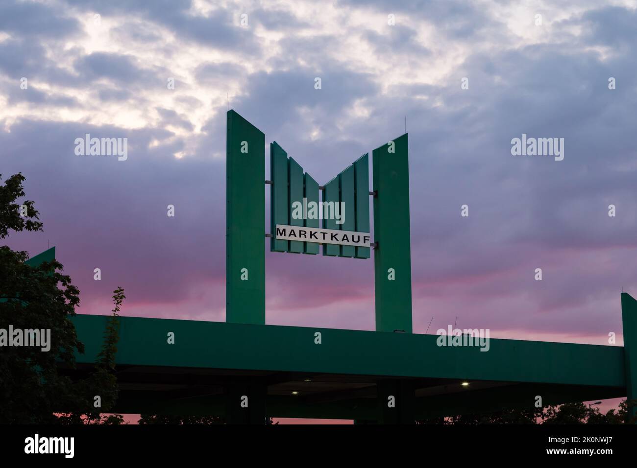 Marktkauf-Logo auf dem Gebäude vor einem Sonnenuntergangshimmel. Dunkles großes M-Zeichen in grüner Farbe des Firmenbrandings. Die Marktkauf Holding. Stockfoto