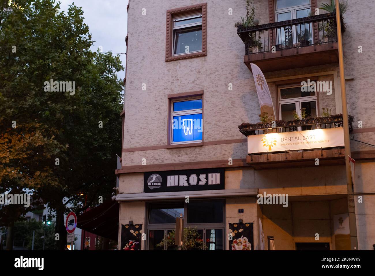 Blau glühender Zahn im Fenster eines Zahnarztes. Werbung mit einem Neonschild in der Stadt. Praxis Dental East in der deutschen Stadt. Gesundheitswesen Stockfoto