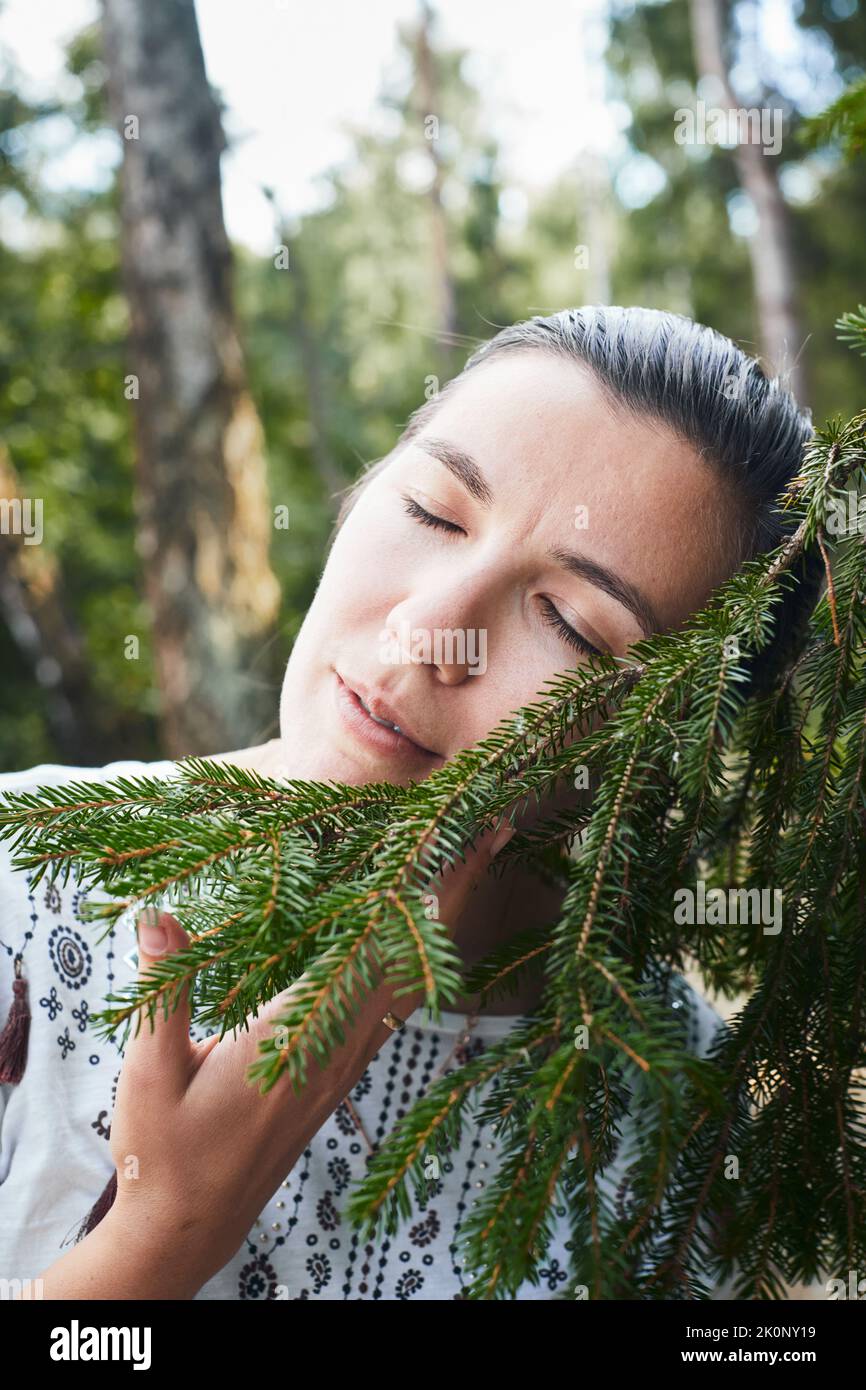 Eine Frau umarmt einen Nadelbaum im Wald. Das Konzept des Lebens in der Nähe von Natur und Wald. Vertikales Foto. Stockfoto