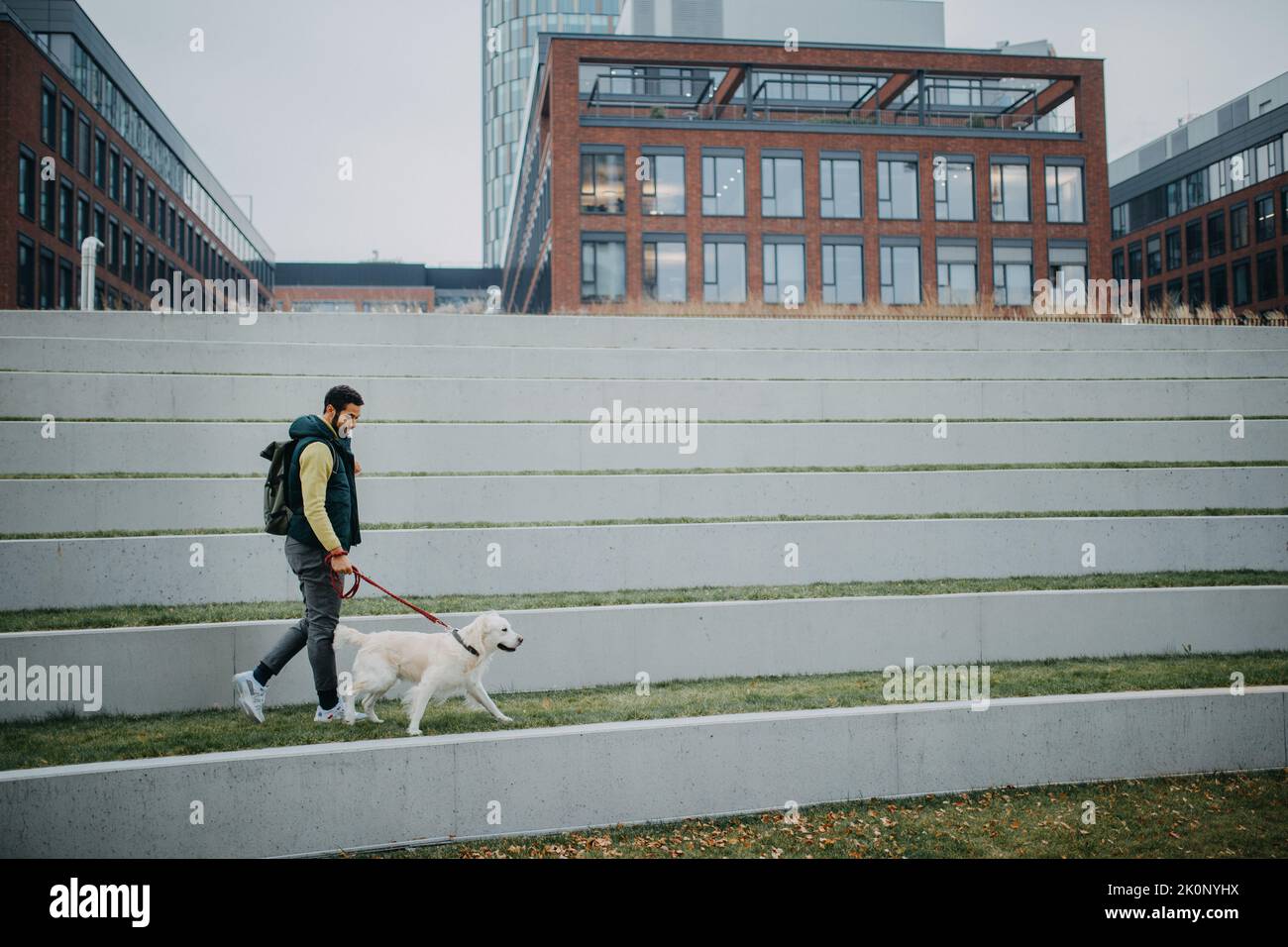 Glücklicher junger Mann, der während des grauen Herbsttages mit seinem Hund in der Stadt unterwegs ist. Stockfoto