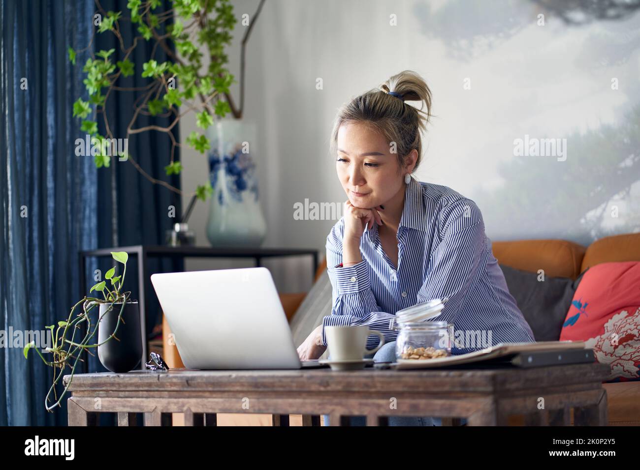Reife professionelle asiatische Frau, die von zu Hause aus auf der Couch sitzt und Laptop-Computer anschaut Stockfoto