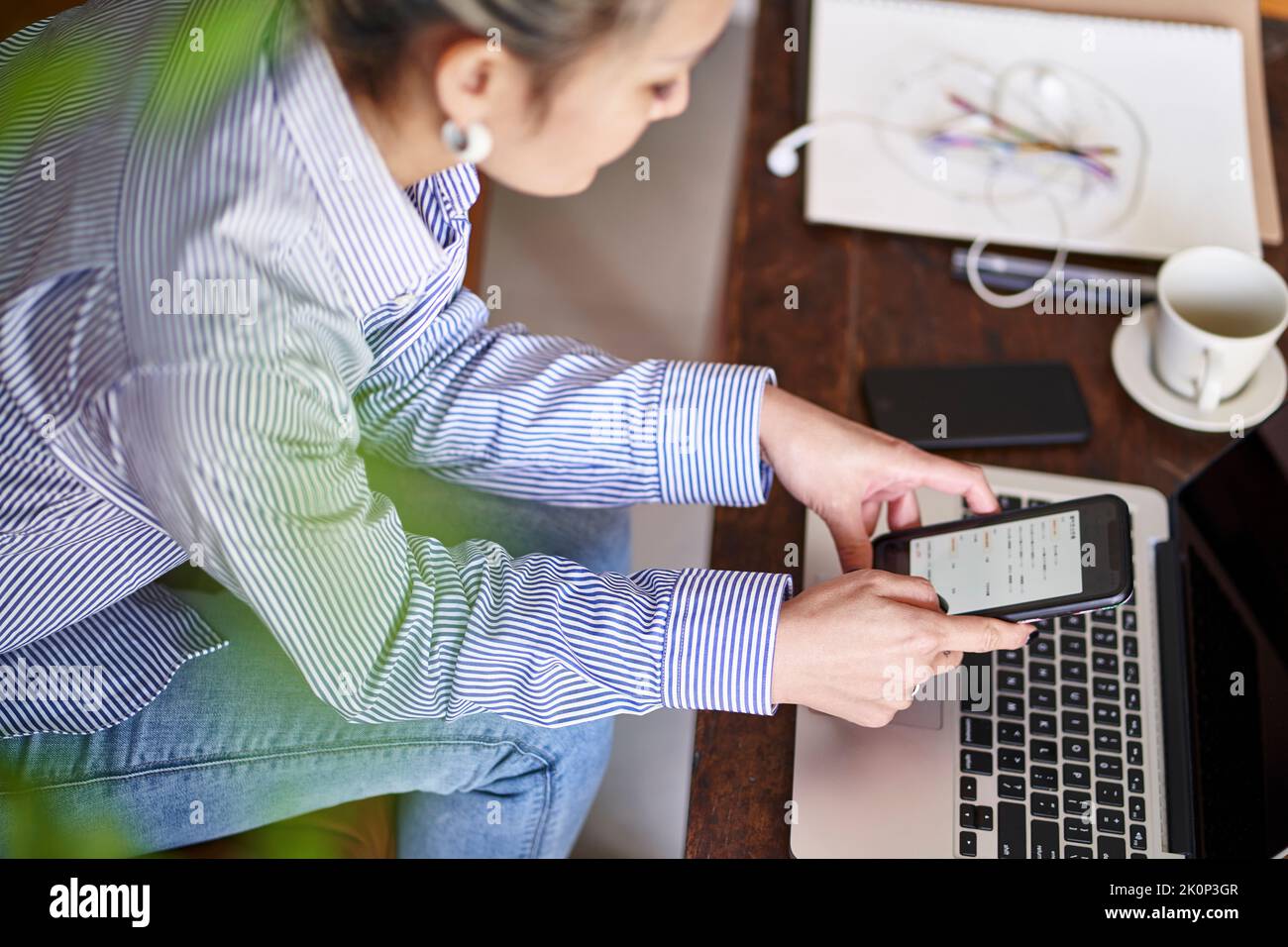 Reife professionelle asiatische Frau, die von zu Hause aus mit Handy und Laptop-Computer High-Angle-Seitenansicht Stockfoto