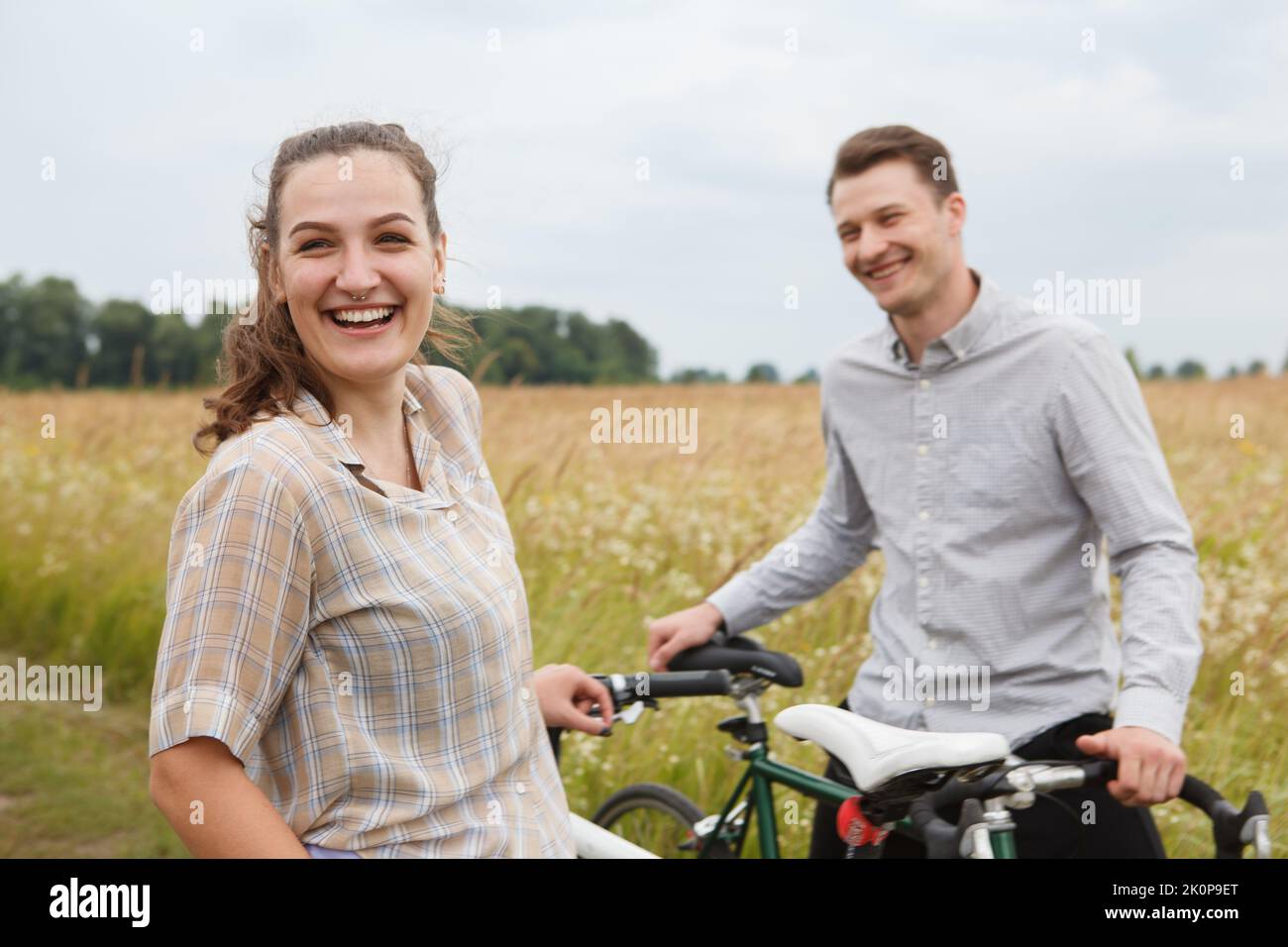 Das glückliche Paar radelt in der Nähe des Feldes. Radfahrer Mann und eine Frau mit Fahrrädern gehen im Sommer in die Nähe der Felder. Stockfoto