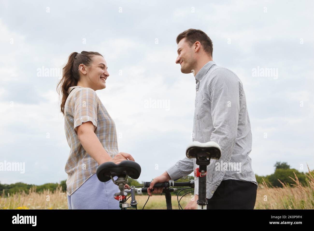 Das glückliche Paar radelt in der Nähe des Feldes. Radfahrer Mann und eine Frau mit Fahrrädern gehen im Sommer in die Nähe der Felder. Stockfoto