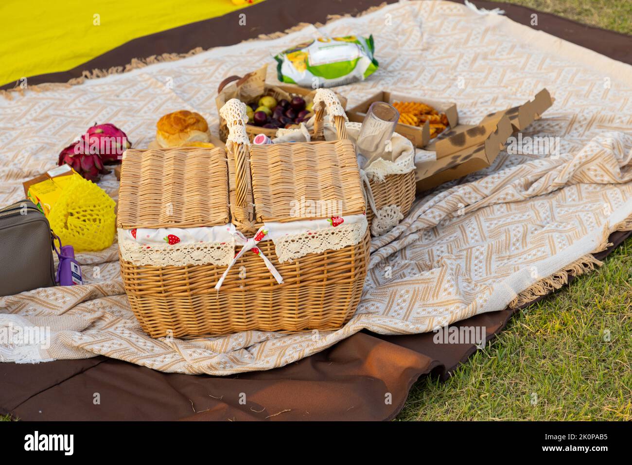Picknickkorb mit Produkten und einer Flasche Wein, Kerzen, Obst auf karierter Decke im Garten, schönes romantisches Picknick im Frühlingspark Stockfoto