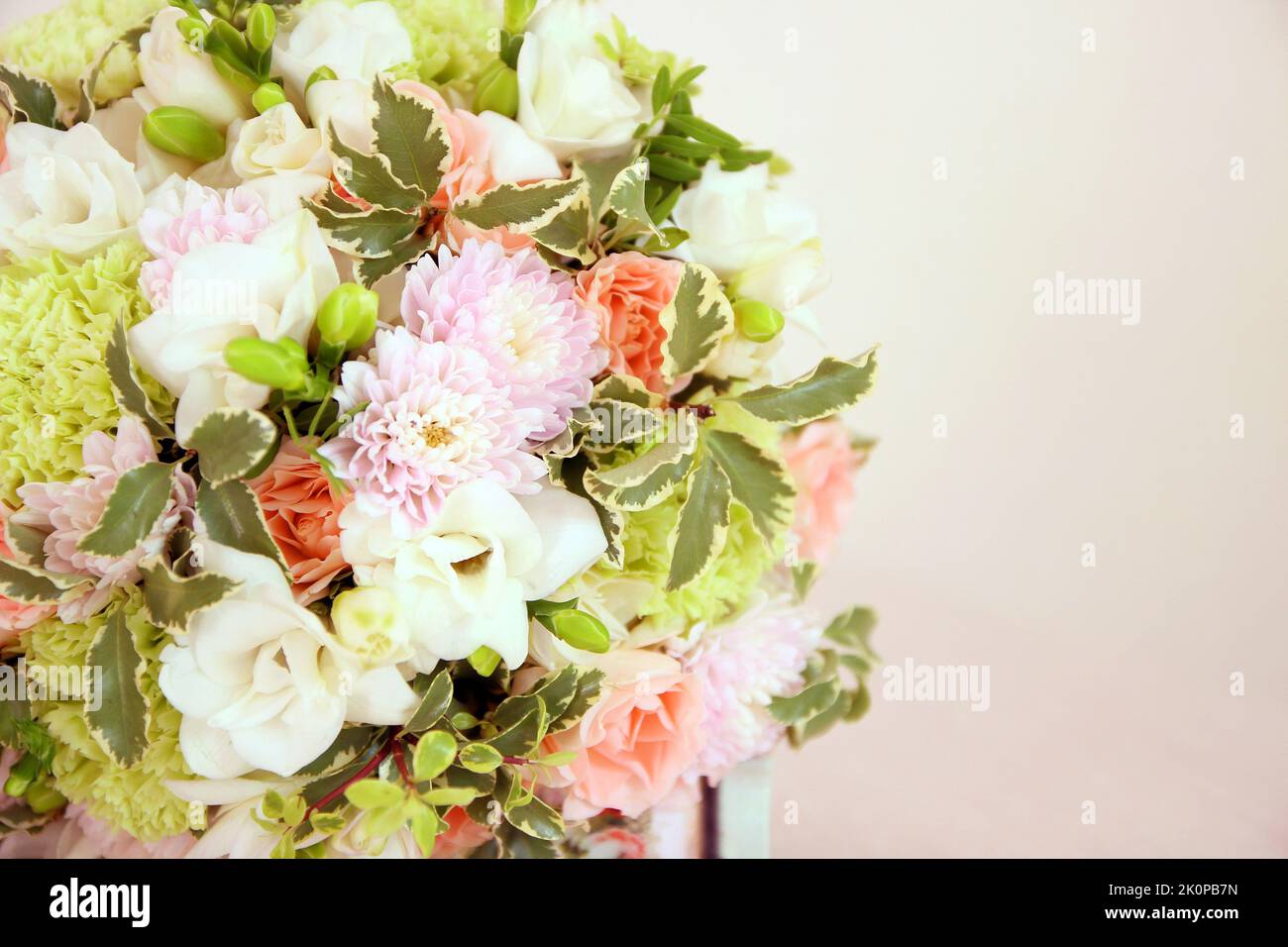 Rundes Bouquet mit weißer Freesia-Blume, grünem Dianthus, Pfirsichrosen, heller Chrysantheme und frischem Grün. Brautstrauß und Holz auf rosa Hintergrund Stockfoto