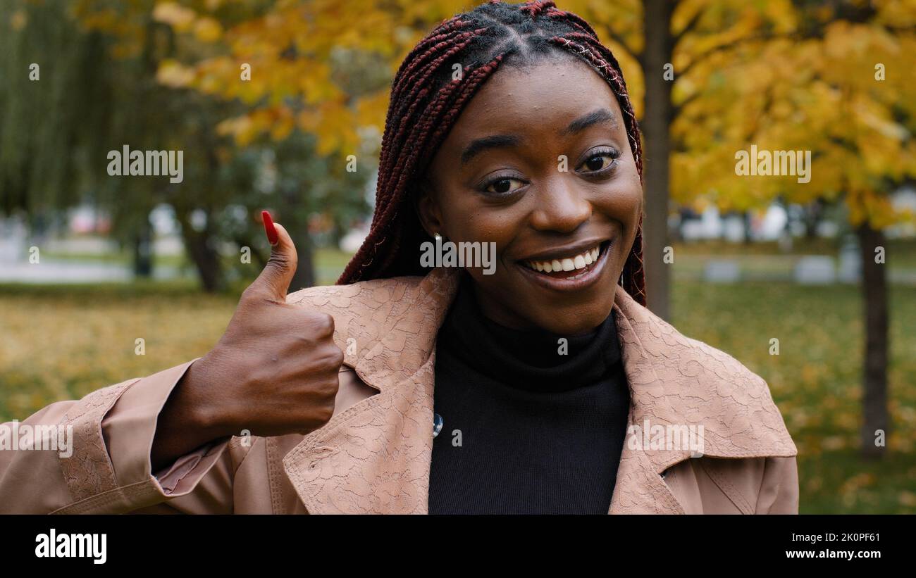 Lächelnde, glückliche junge afroamerikanische Frau, die die Kamera anschaut und den Daumen nach oben zeigt, wenn sie eine Serviceempfehlung gibt, positives Feedback gibt, fühlt sich zufrieden Stockfoto