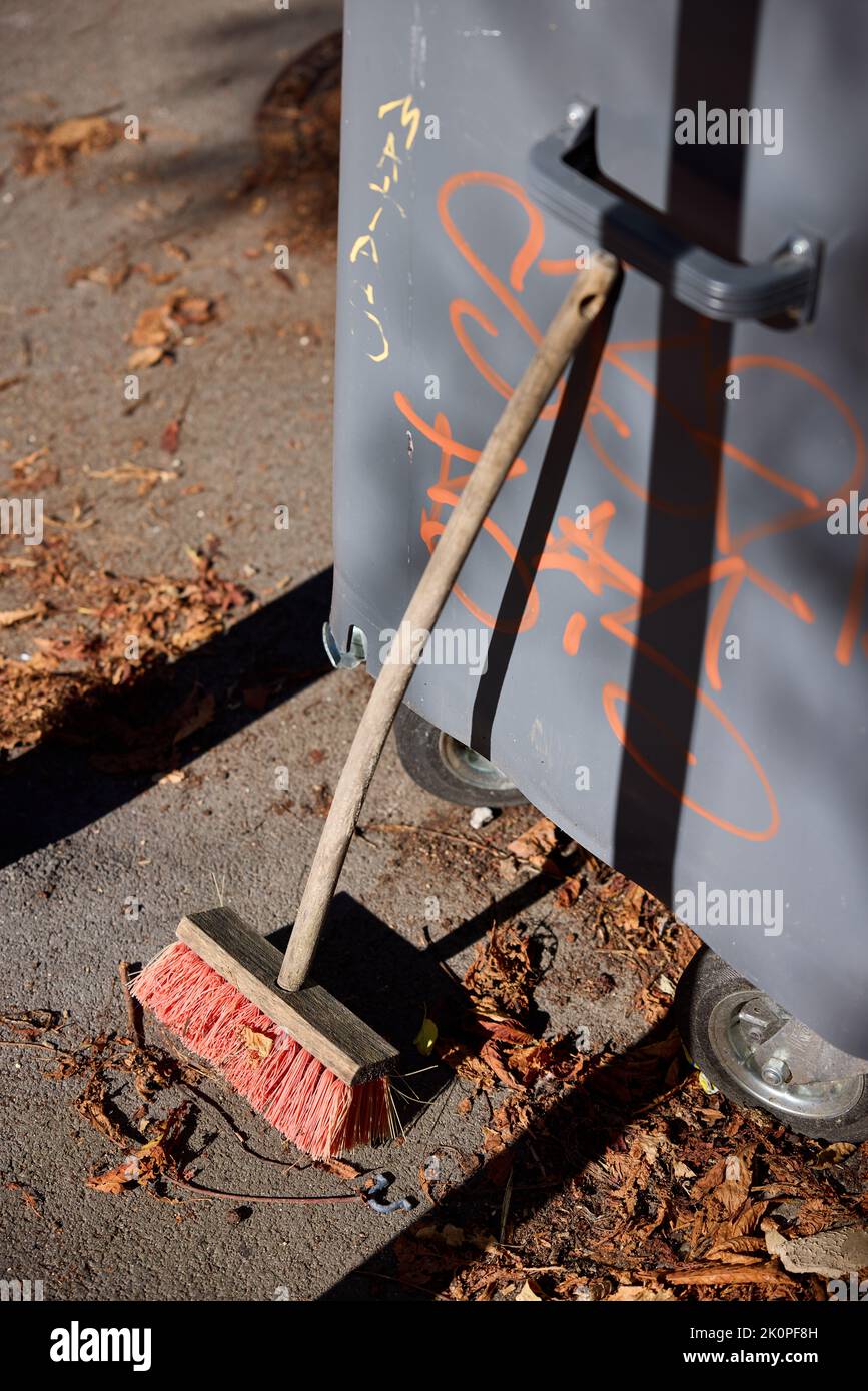 Besen ruht gegen Abfallbehälter, braune Blätter auf dem Boden Stockfoto