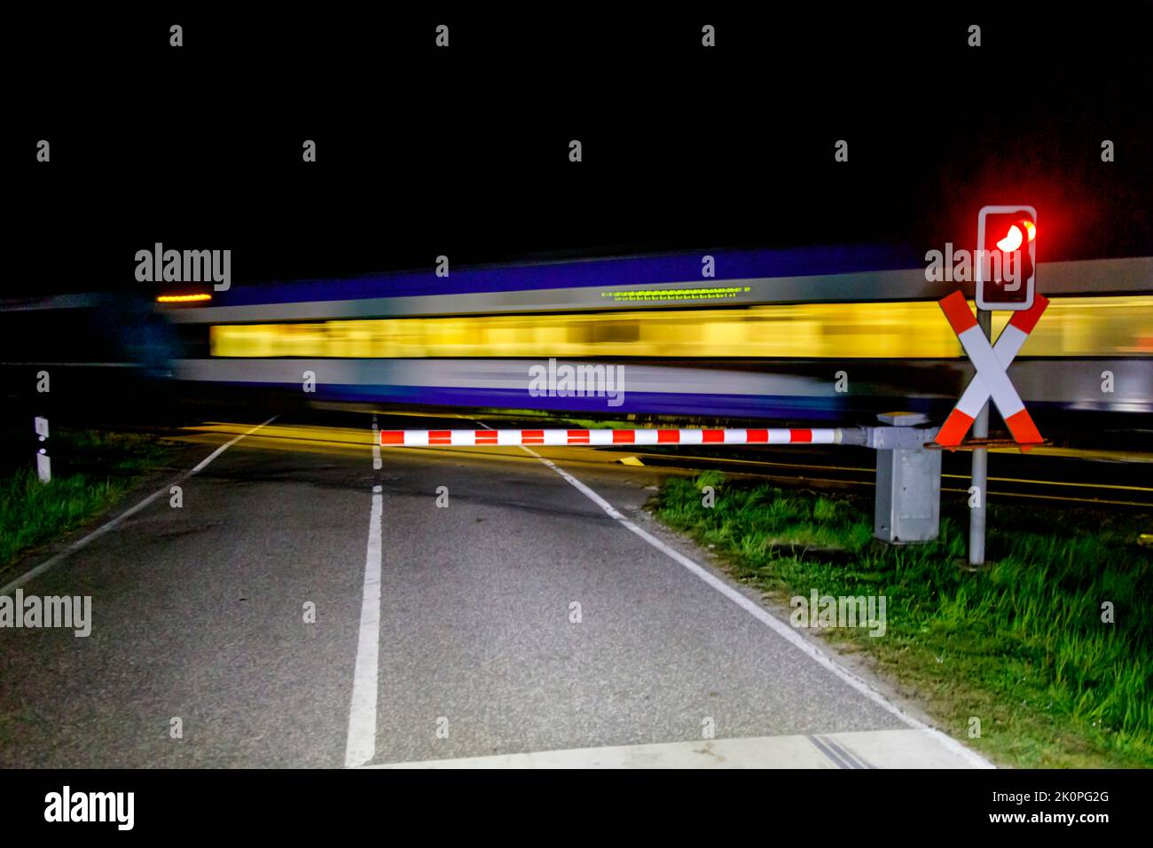 Geschlossener Bahnübergang, vorbei am Regionalzug in der Nacht Stockfoto