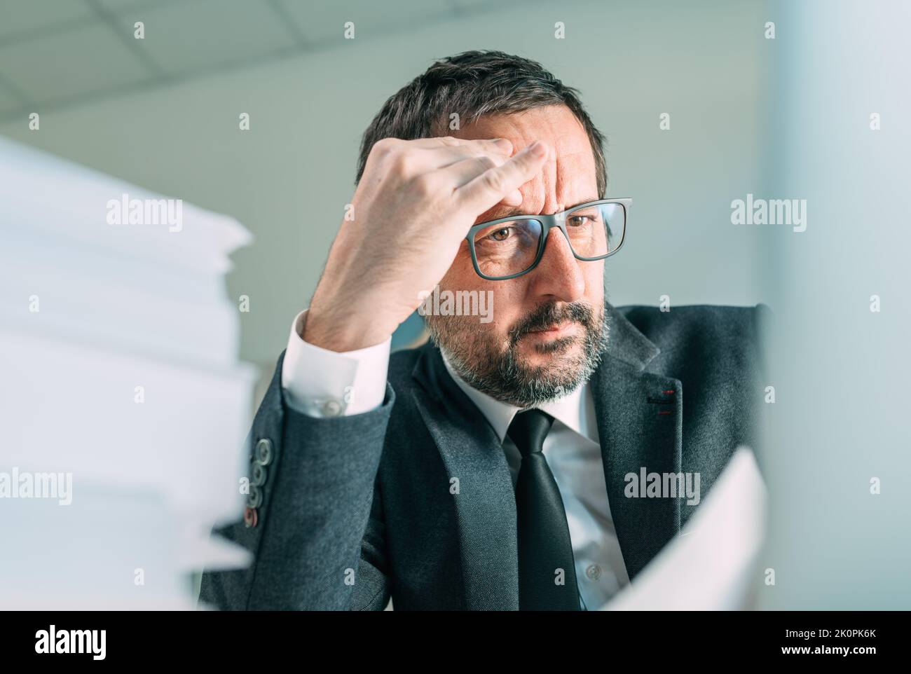 Ernste Geschäftssituation, die Kopfschmerzen im Büroleben verursacht, besorgter Geschäftsmann, der auf den Laptop-Bildschirm schaut und denkt, selektiver Fokus Stockfoto