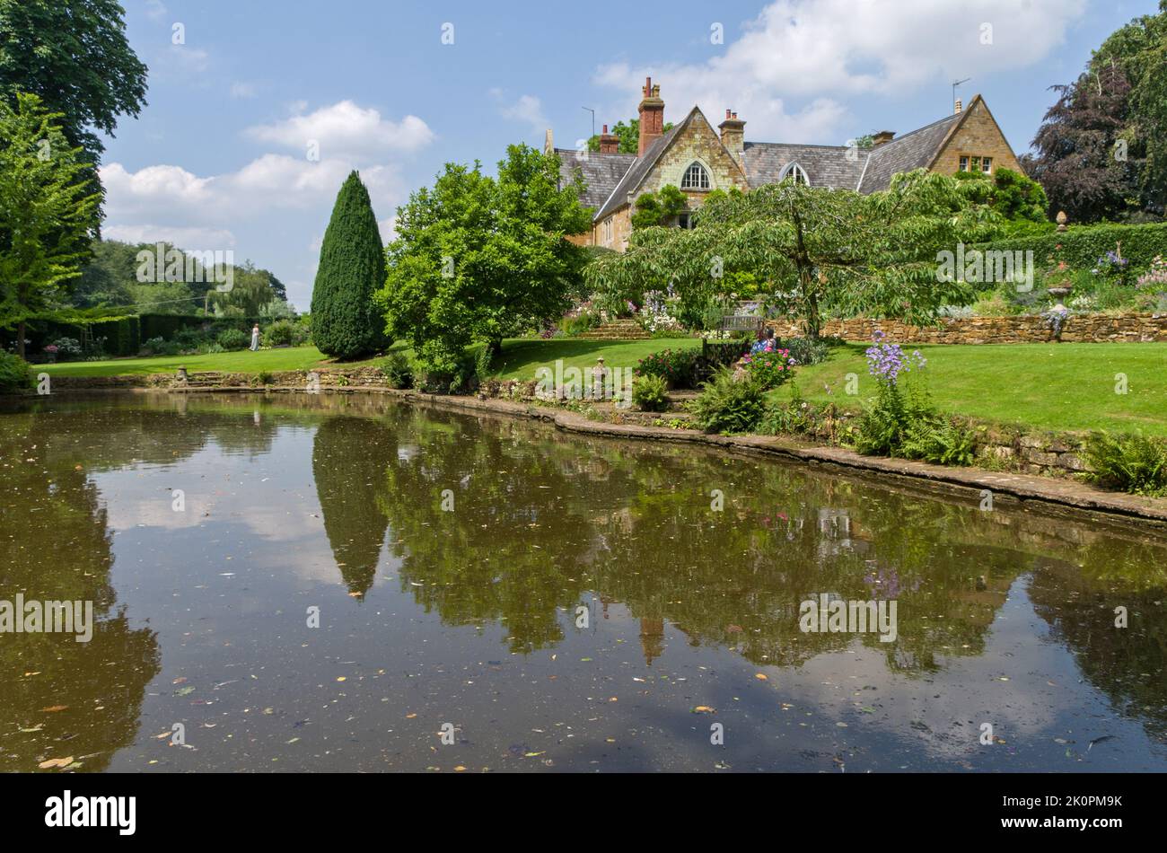 Ein Sommerblick über den Ziersee zum Herrenhaus, Coton Manor Gardens, in der Nähe von Guilsborough, Northamptonshire, Großbritannien Stockfoto