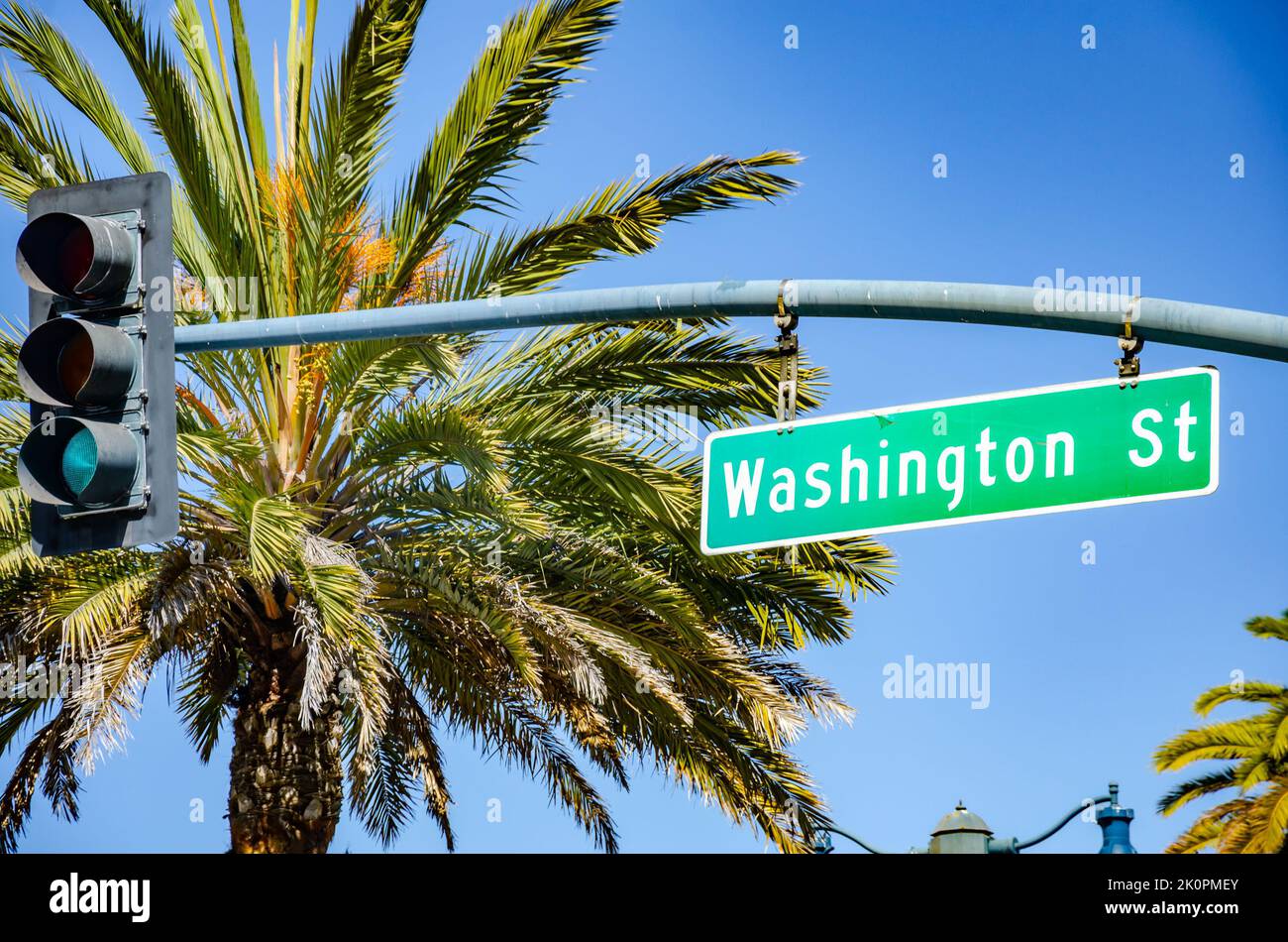 Ein Straßenschild für die Washington Street, das an der Kreuzung einer Ampel in San Francisco mit Palmen und blauem Himmel im Hintergrund hängt Stockfoto