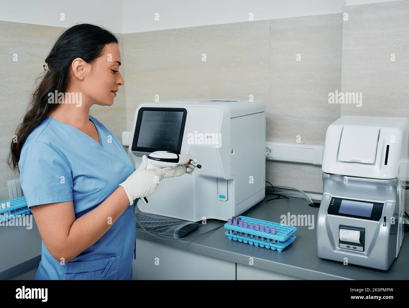 Laborarbeiterin scannt den Barcode des Reagenzschlauchs mit Blut auf ihrem Arbeitsplatz in der Nähe einer medizinischen Forschungsmaschine Stockfoto