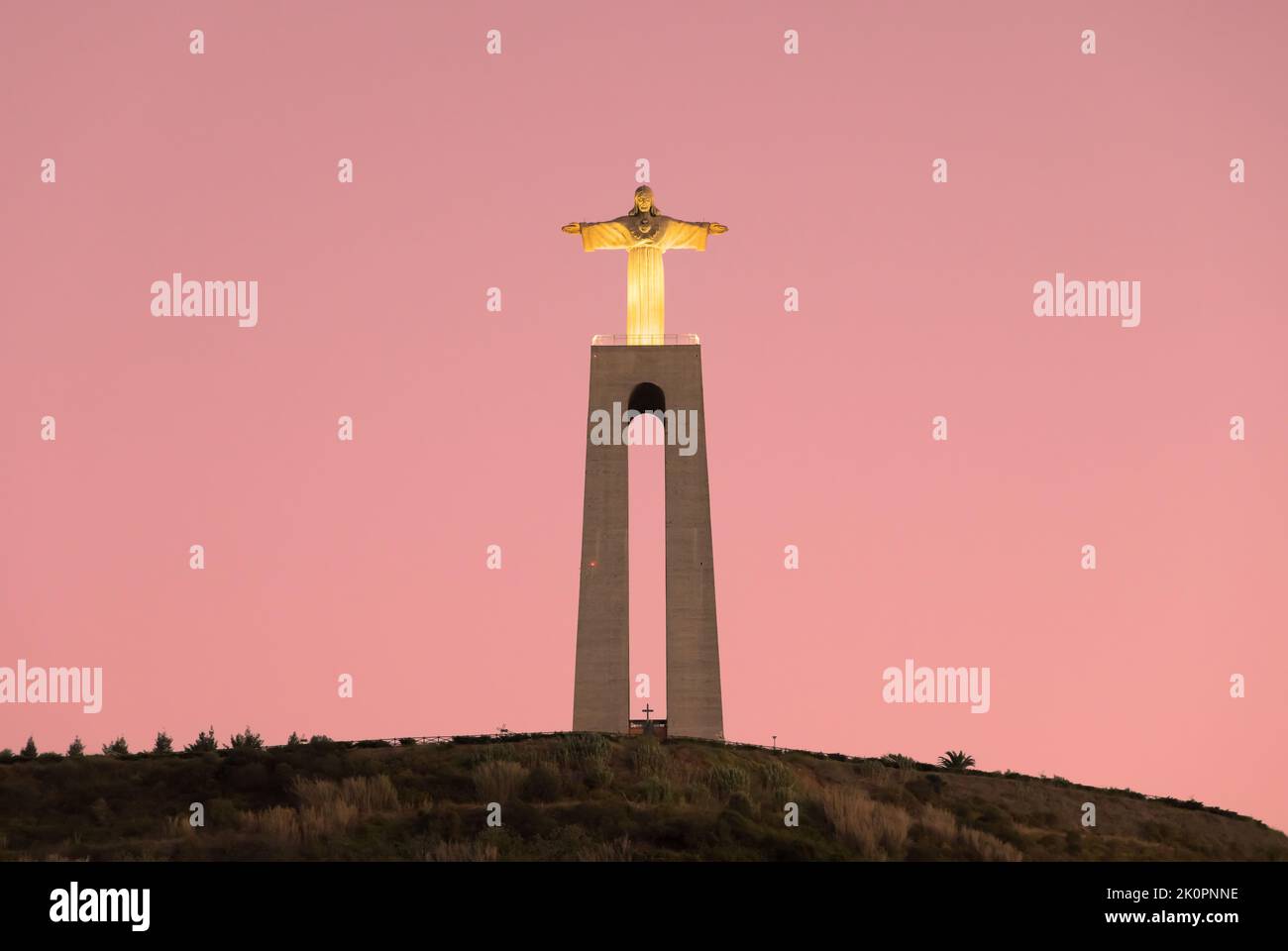 Christus der König, Cristo Rei Statue in Almada, Lissabon, Portugal. Das erleuchtete Christusdenkmal, das während des Sonnenuntergangs vom Fluss Tejo aus gesehen wurde. Stockfoto