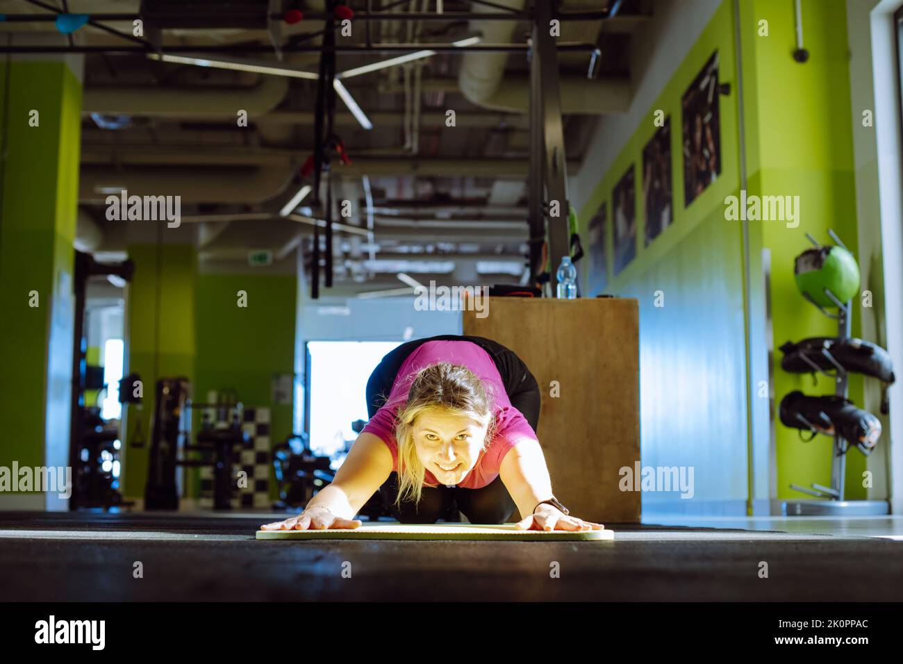 Fröhliches Mädchen liegt auf den Knien und lehnt sich mit ausgestreckten Armen auf der Matte im Fitnessstudio. Junge Frau mit Lächeln tun Stretching-Training. Schulung in Stockfoto