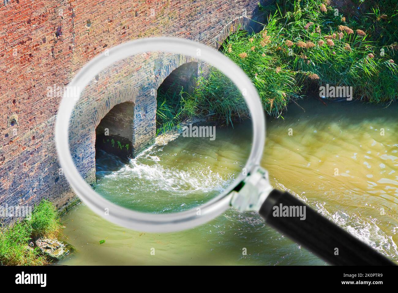 Gefährlich giftig verschmutztes Wasser fließt in Richtung Fluss - Konzeptbild durch eine Lupe gesehen. Stockfoto