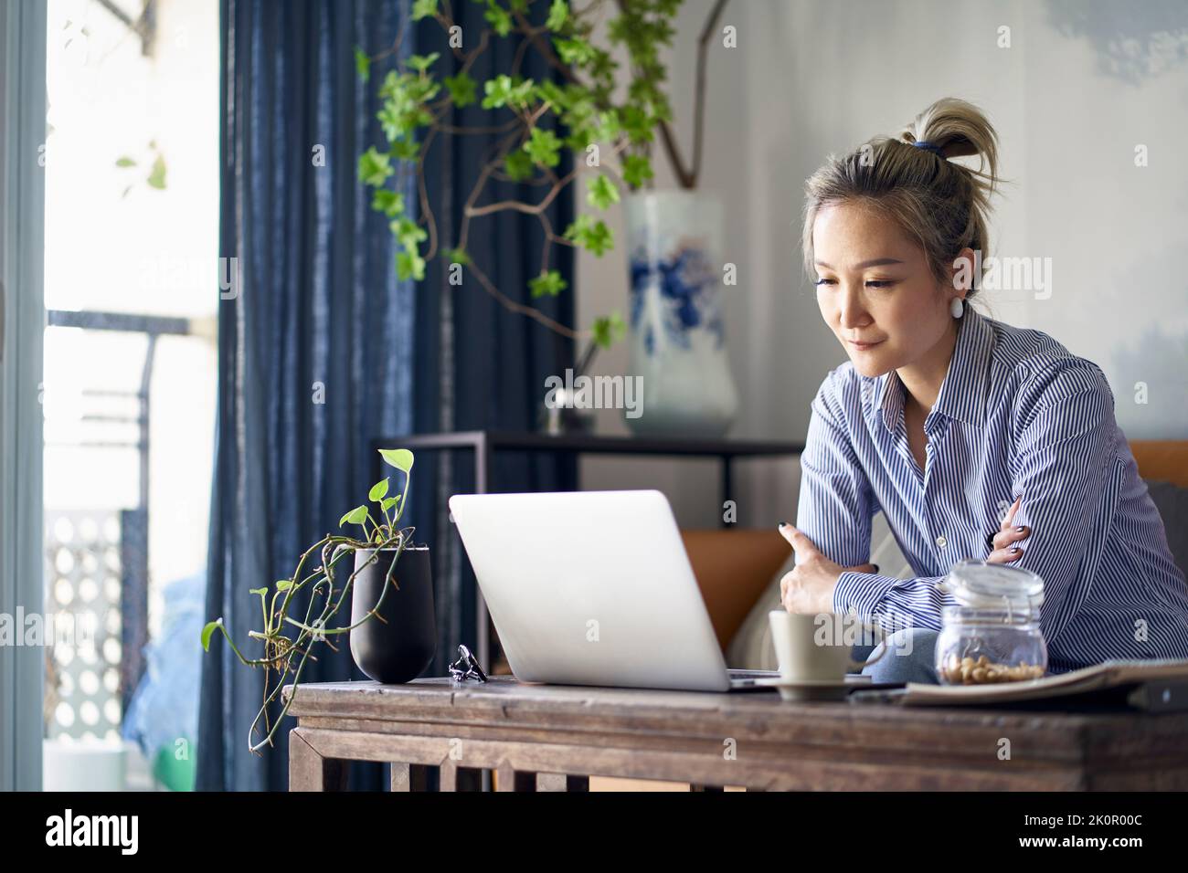 Reife professionelle asiatische Frau, die von zu Hause aus auf der Couch sitzt und Laptop-Computer anschaut Stockfoto