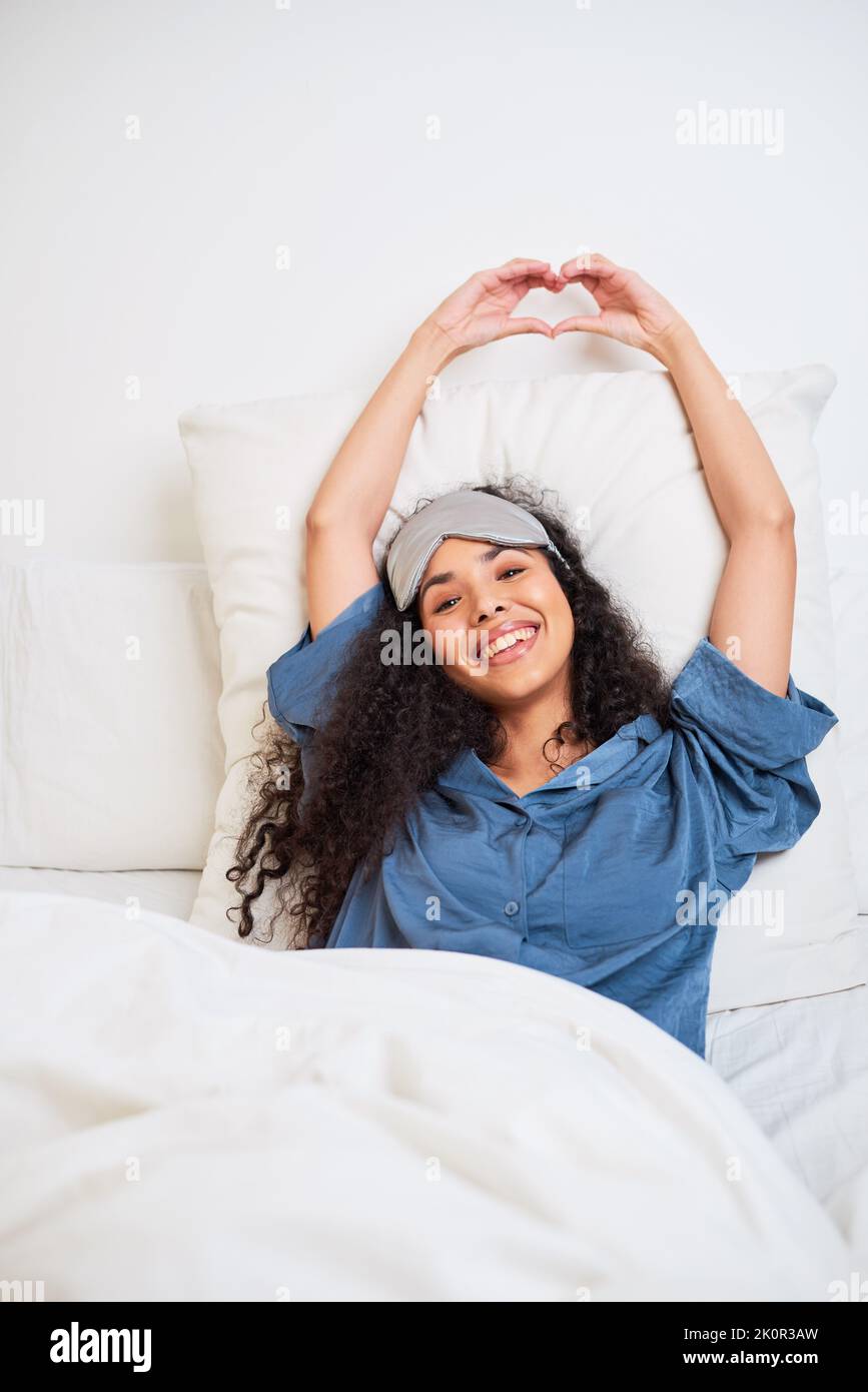 Eine schöne junge, multiethnische Frau macht Herzform mit aufwachenden Händen Stockfoto