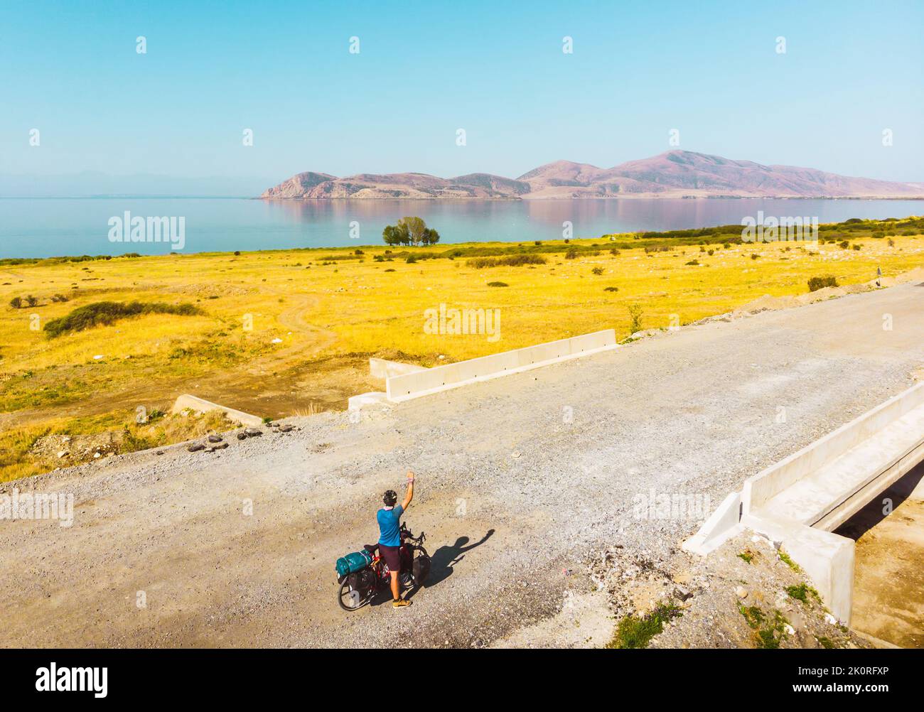 Luftaufnahmen-Solo-Radfahrer Fahrrad-Touring stehen aufgeregt Hände oben am See in heißen Sommertag auf Sommerradurlaub. Abenteuerlich aktiv gesund Urlaub in Stockfoto