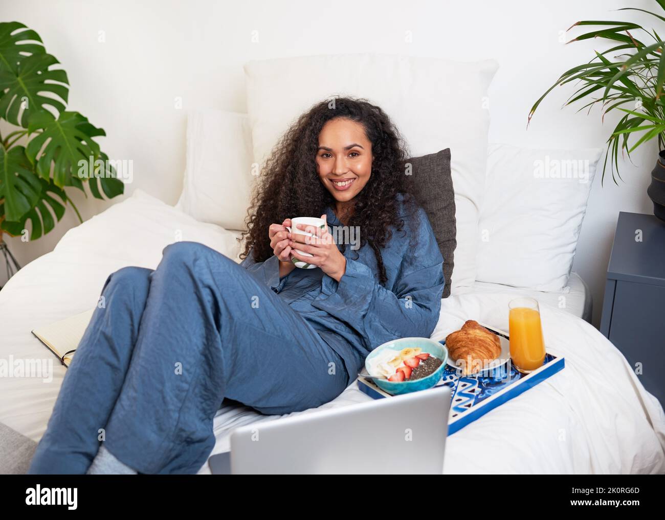 Eine junge Frau schaut sich Filme im Bett an, während sie zur Selbstversorgung Brunch hat Stockfoto