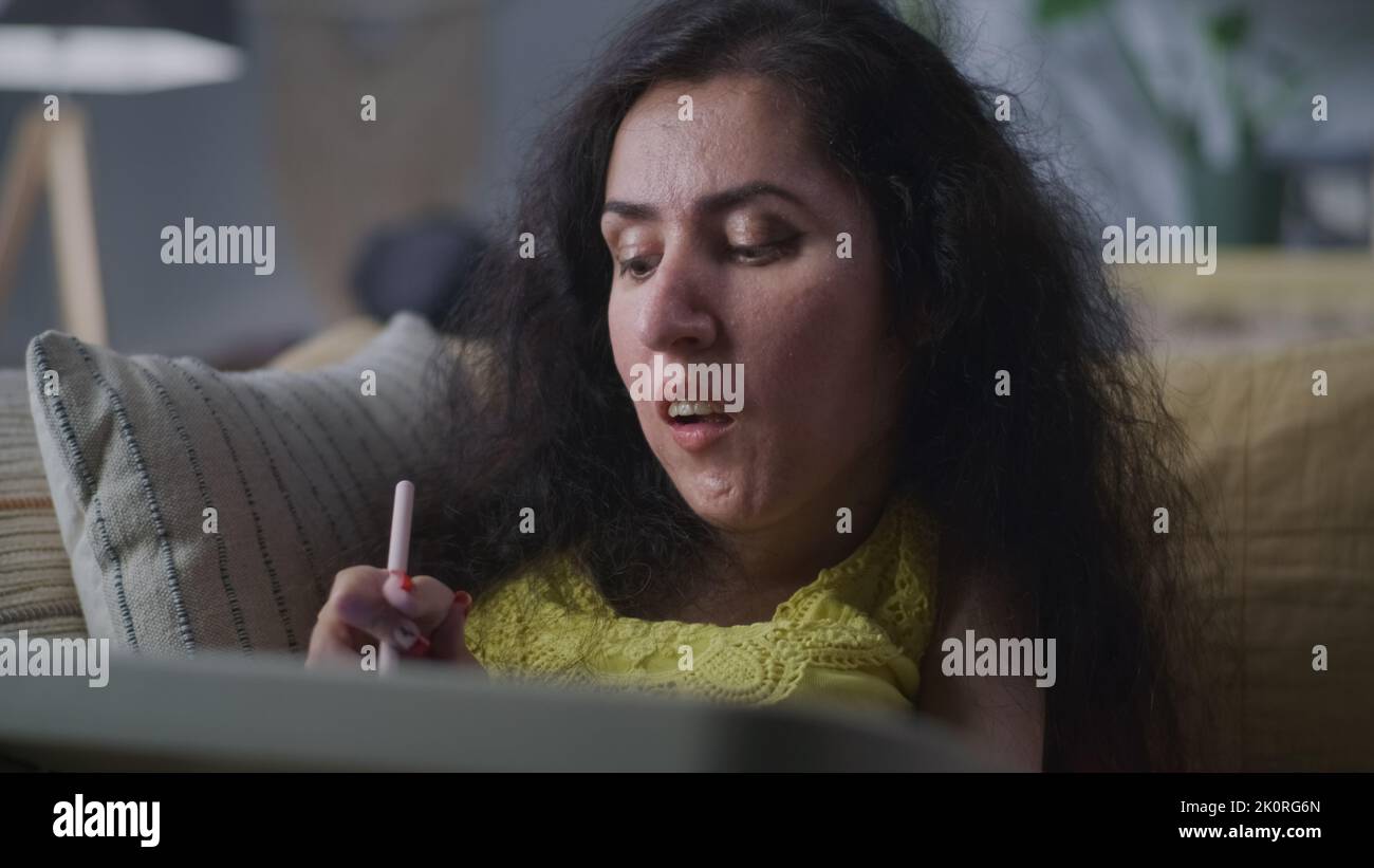 Frau mit einer körperlichen Behinderung, die digitalen Bleistift zum Zeichnen verwendet, während sie auf einem Sofa am Tisch in einem gemütlichen Zuhause sitzt Stockfoto