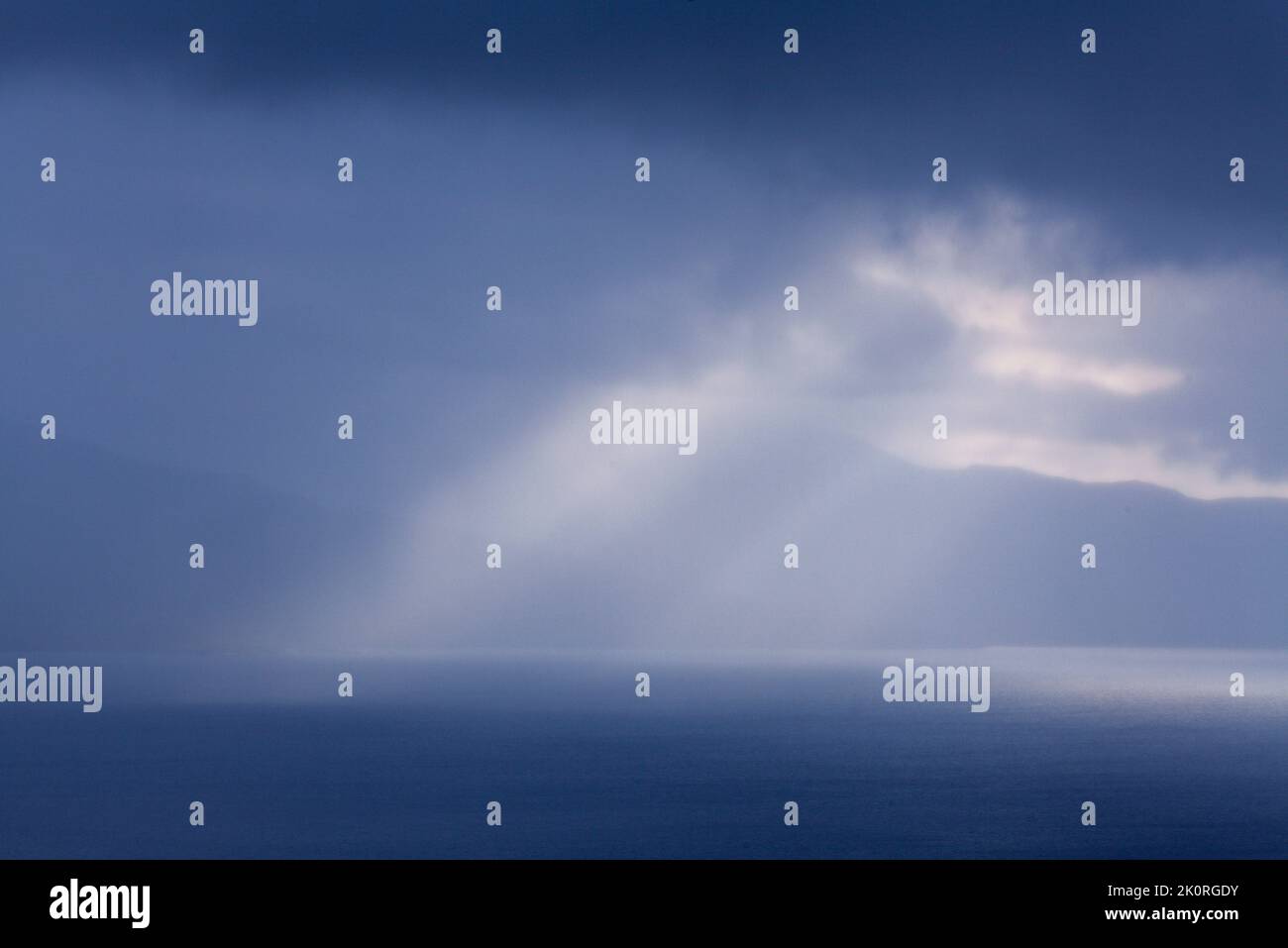 September und Sonnenstrahlen passieren regnerische Wolken. See auf dieser Seite und Berg im Hintergrund. Stockfoto