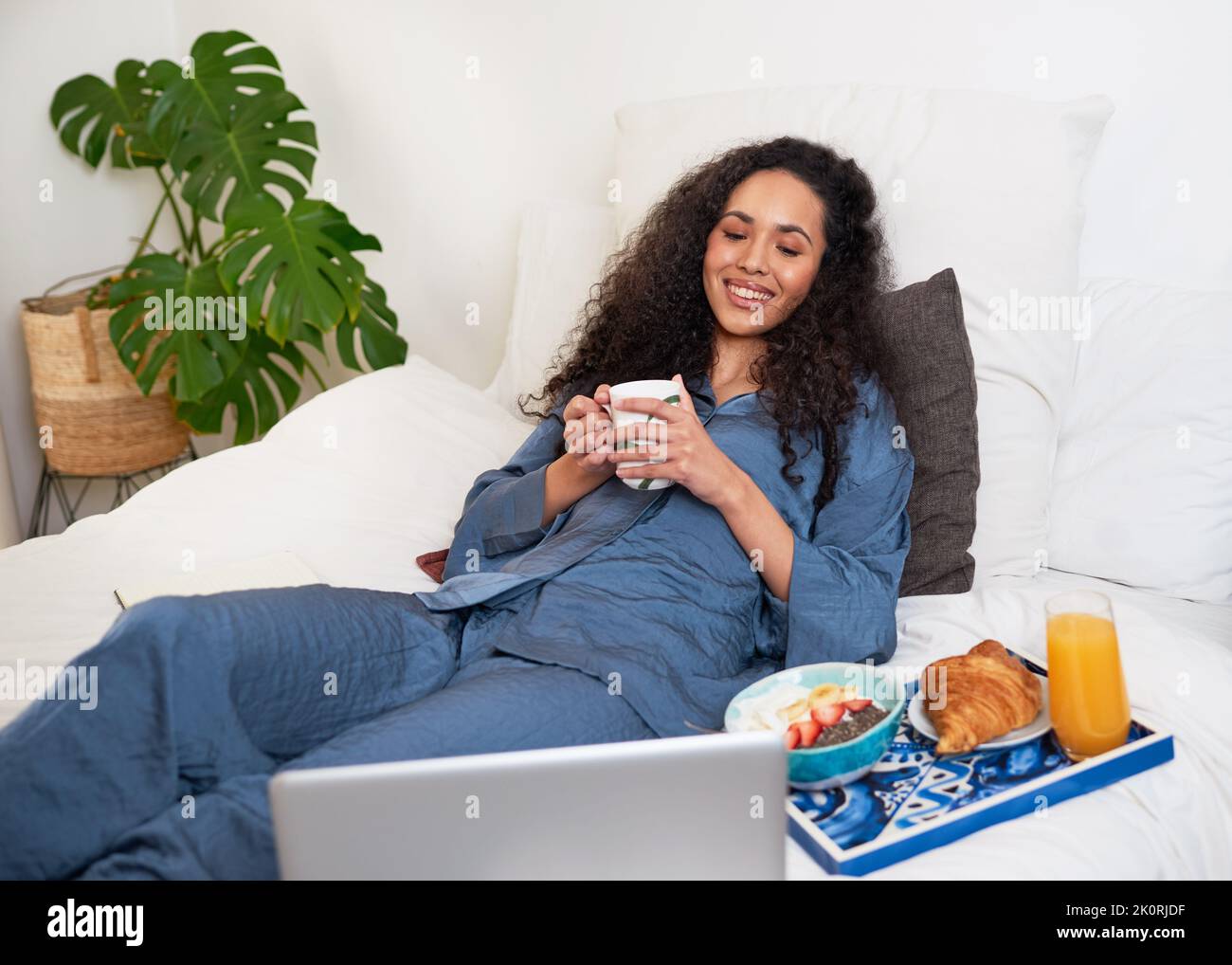 Eine junge Frau schaut sich Filme im Bett an, während sie zur Selbstversorgung Brunch hat Stockfoto