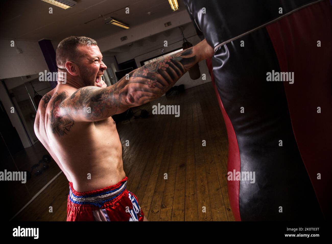 Erwachsener Rüde gibt einem Boxsack im Fitnessstudio einen kräftigen richtigen Schlag. Stockfoto