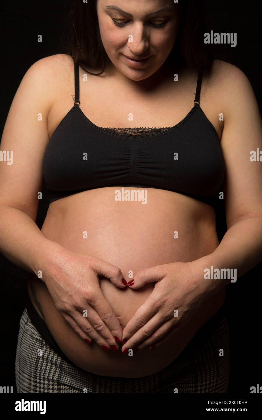 Junge Brünette Frau, die auf ihre große Baby-Beule herunterschaut, Studiolicht verwendet. Stockfoto