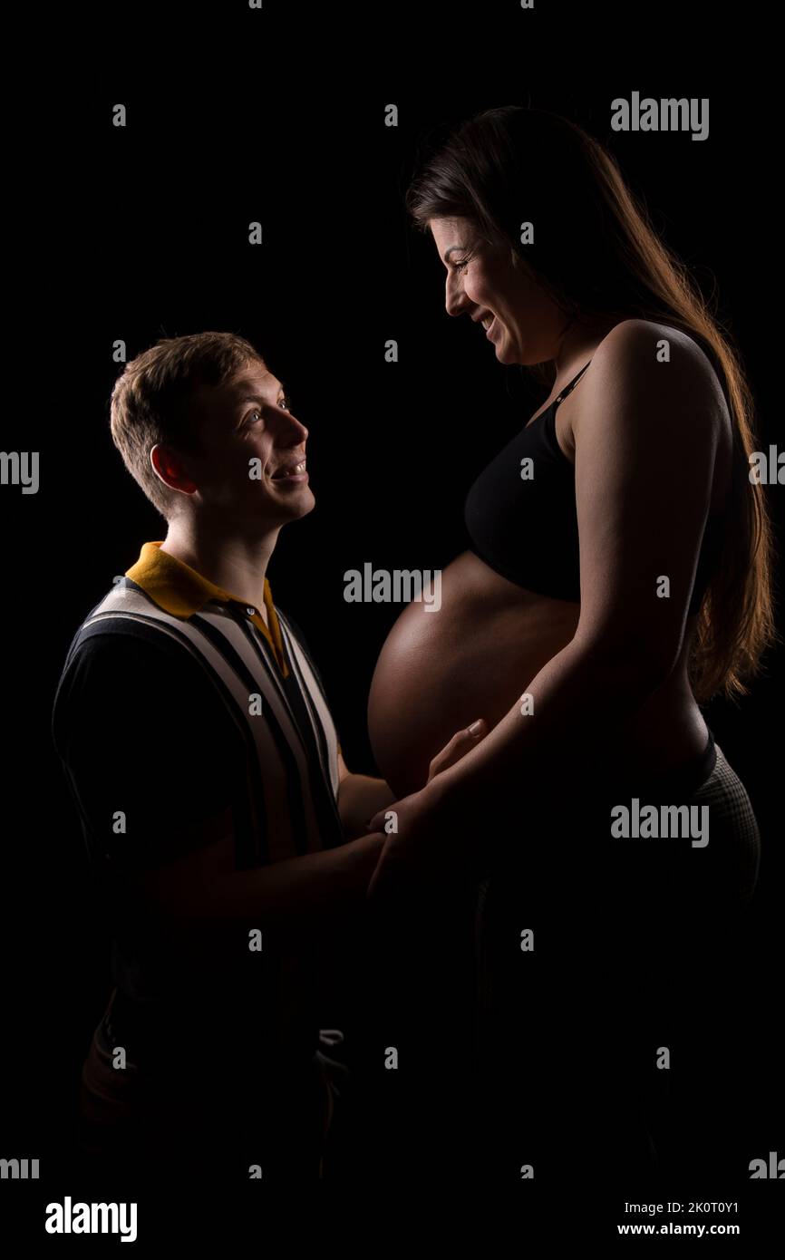 Junge Eltern, die sich liebevoll angucken, während sie dort ungeborenes Kind in der Babybump der Mutter umarmen. Stockfoto