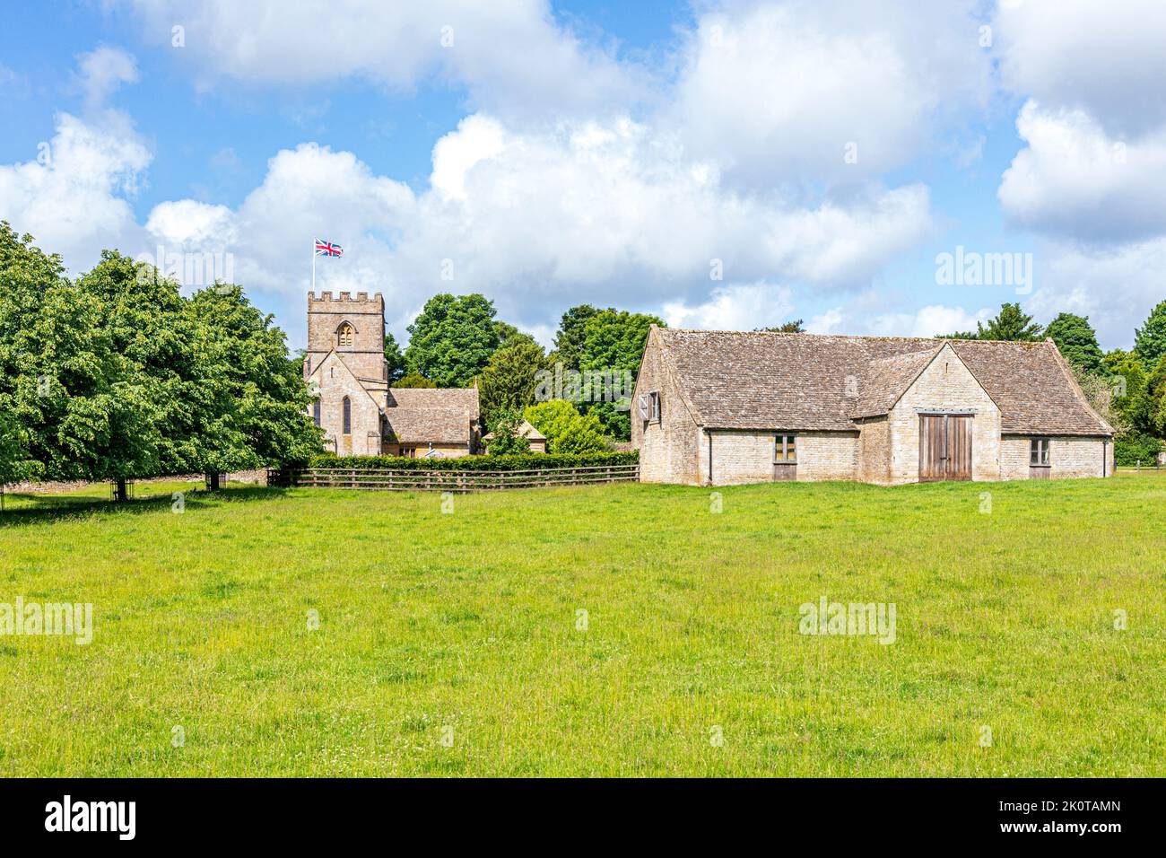 Die normannische Kirche St. Michael and All Angels und eine Scheune aus dem 18.. Jahrhundert im Cotswold-Dorf Guiting Power, Gloucestershire, Großbritannien Stockfoto