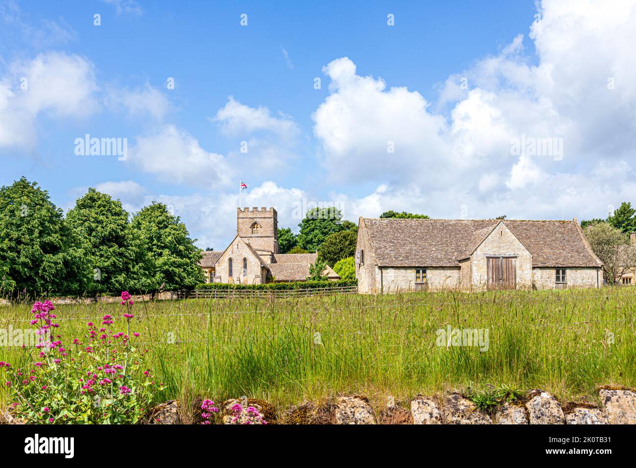 Die normannische Kirche St. Michael and All Angels und eine Scheune aus dem 18.. Jahrhundert im Cotswold-Dorf Guiting Power, Gloucestershire, Großbritannien Stockfoto