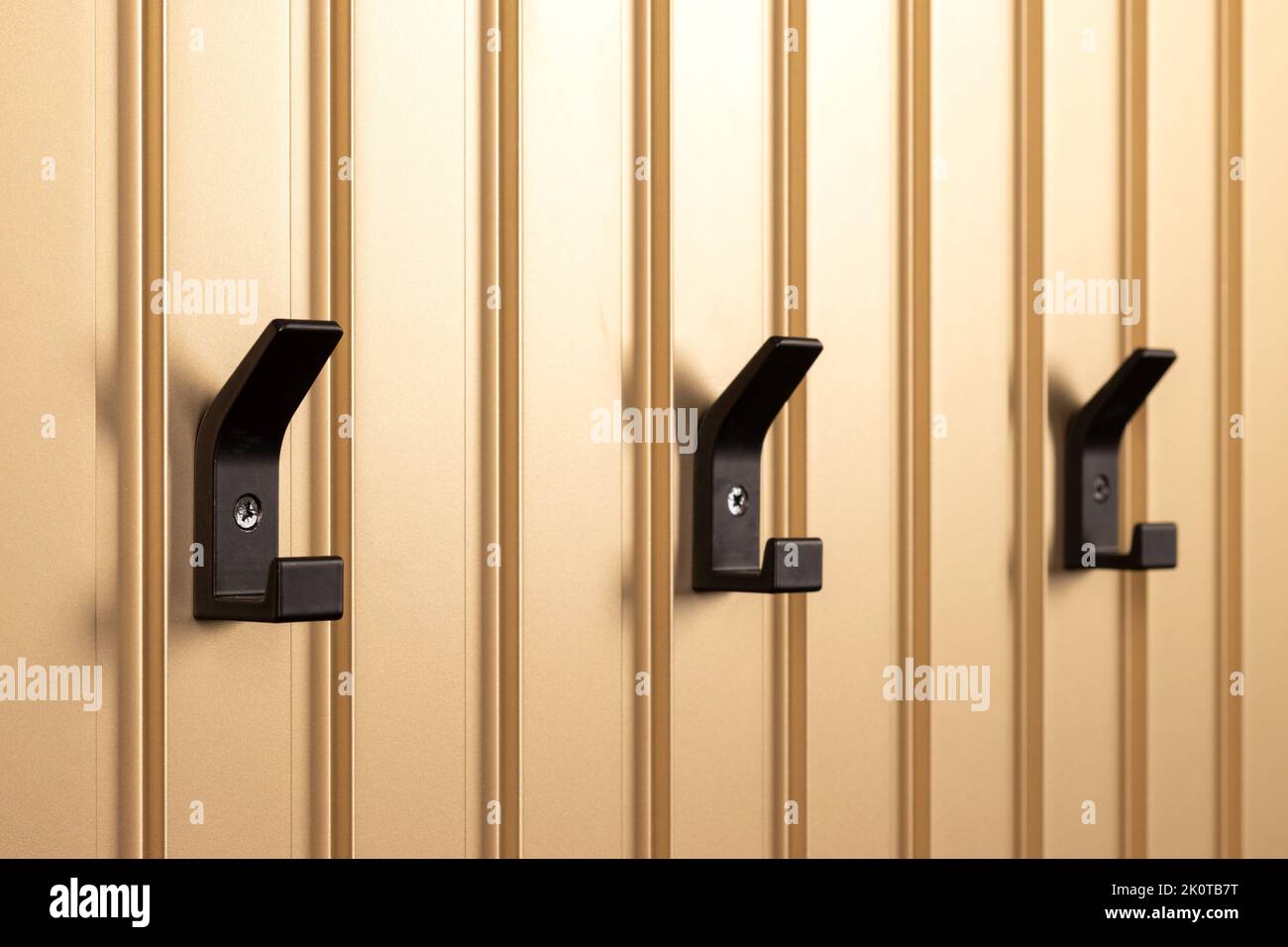 Schwarze moderne Kleiderbügel, Kleiderhaken an der goldenen Wandschlosung. Selektiver Fokus Stockfoto